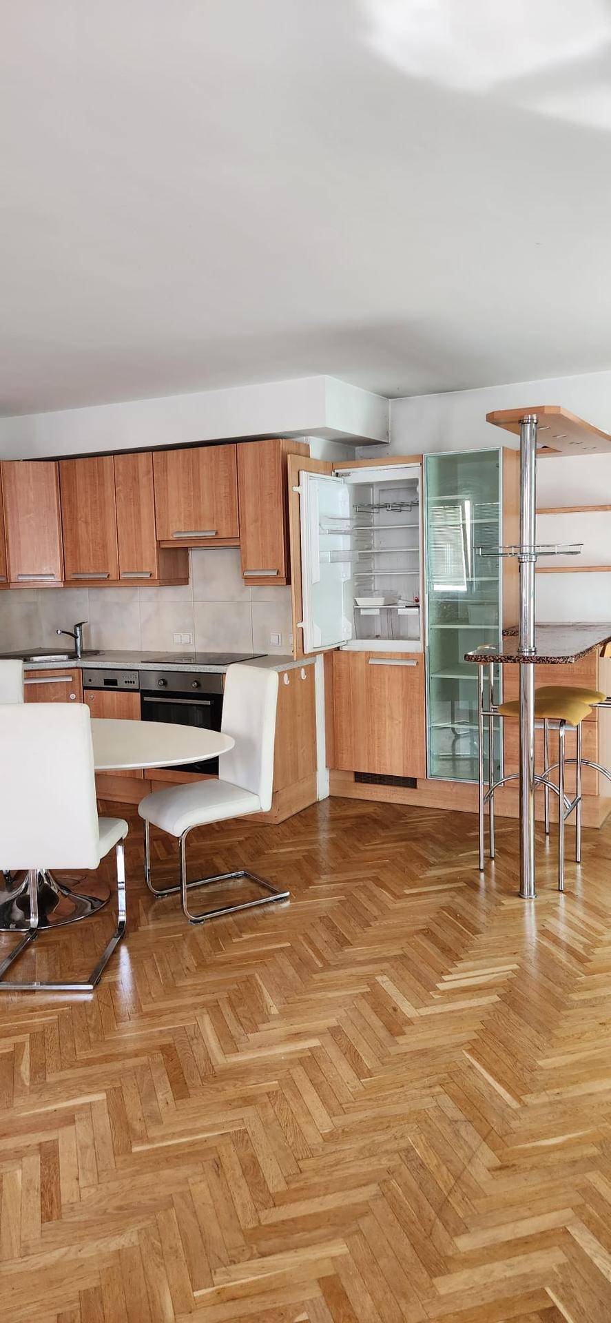 Offene Küche mit Holzschränken, integrierten Geräten und einem Essbereich mit Fischgrätparkettboden.