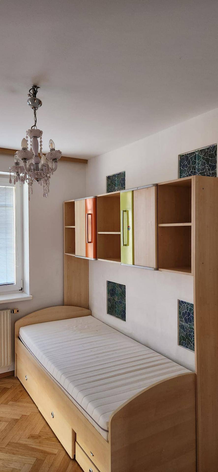 Schlafzimmer mit Einzelbett, integrierten Regalen und einem Fenster, das natürliches Licht hereinlässt.