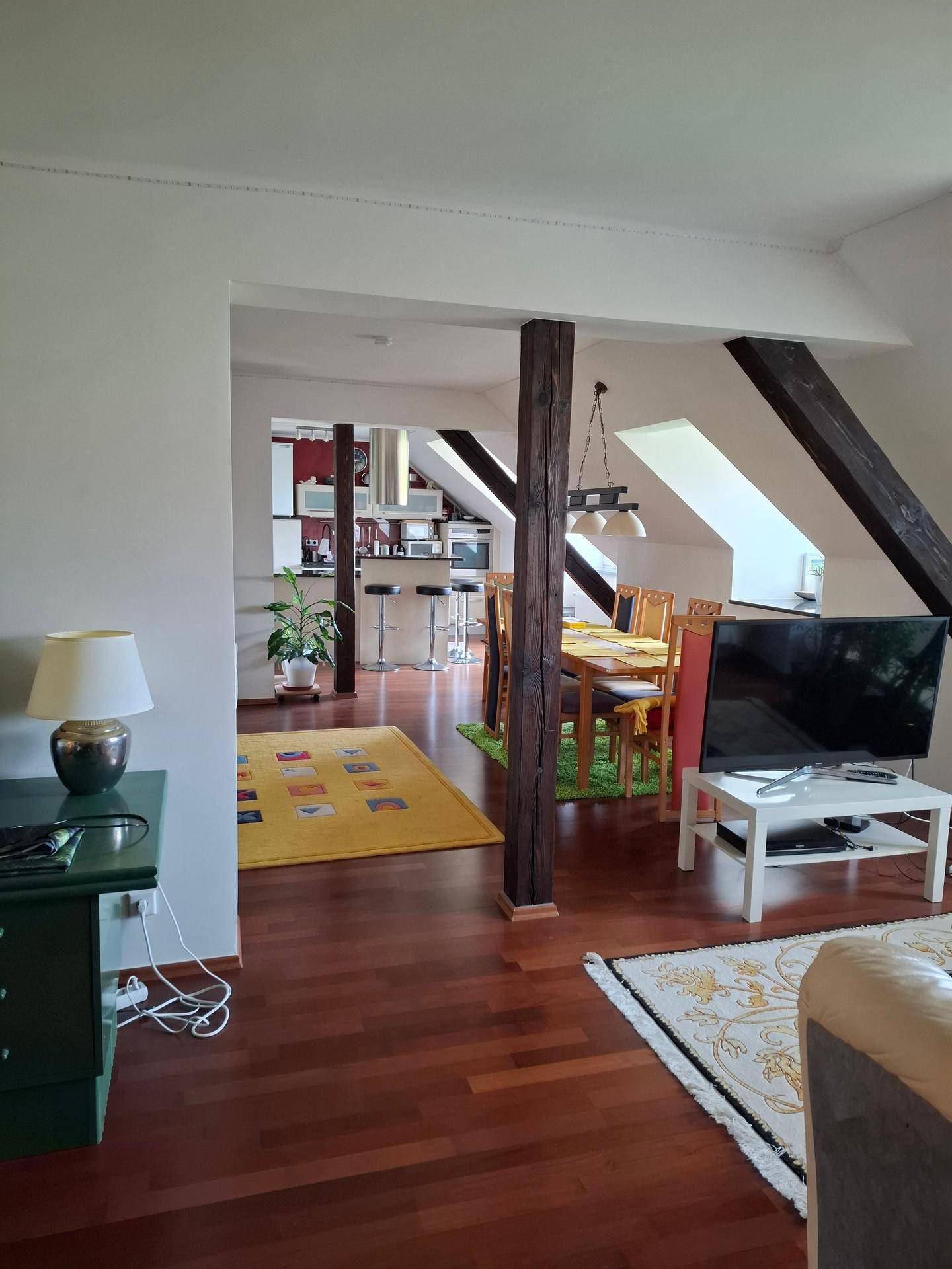 Offener Wohn- und Essbereich mit dunklem Holzboden und sichtbaren Holzbalken.
