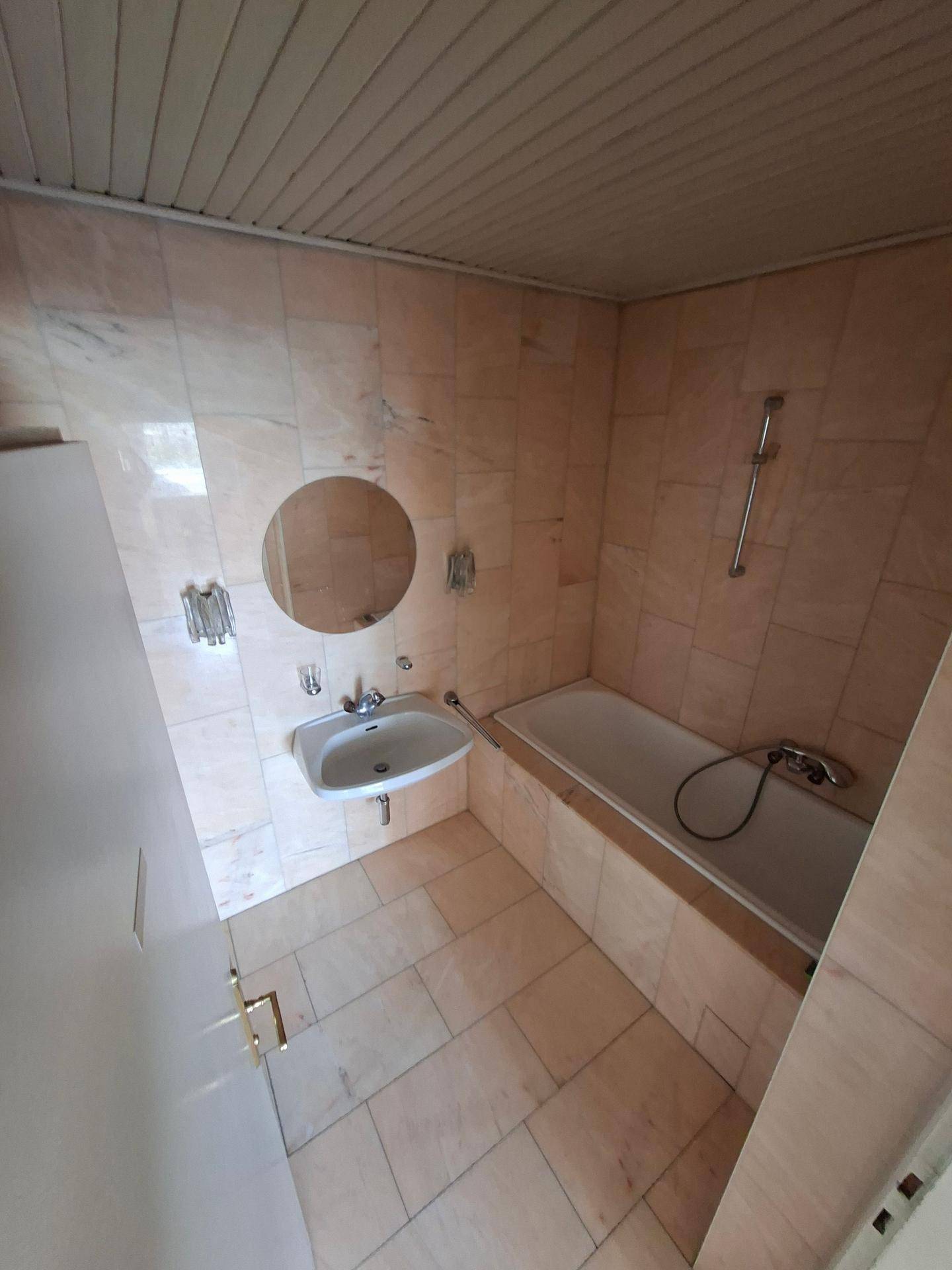 Badezimmer mit Badewanne, Waschbecken und beigefarbenen Fliesen an Wänden und Boden.
