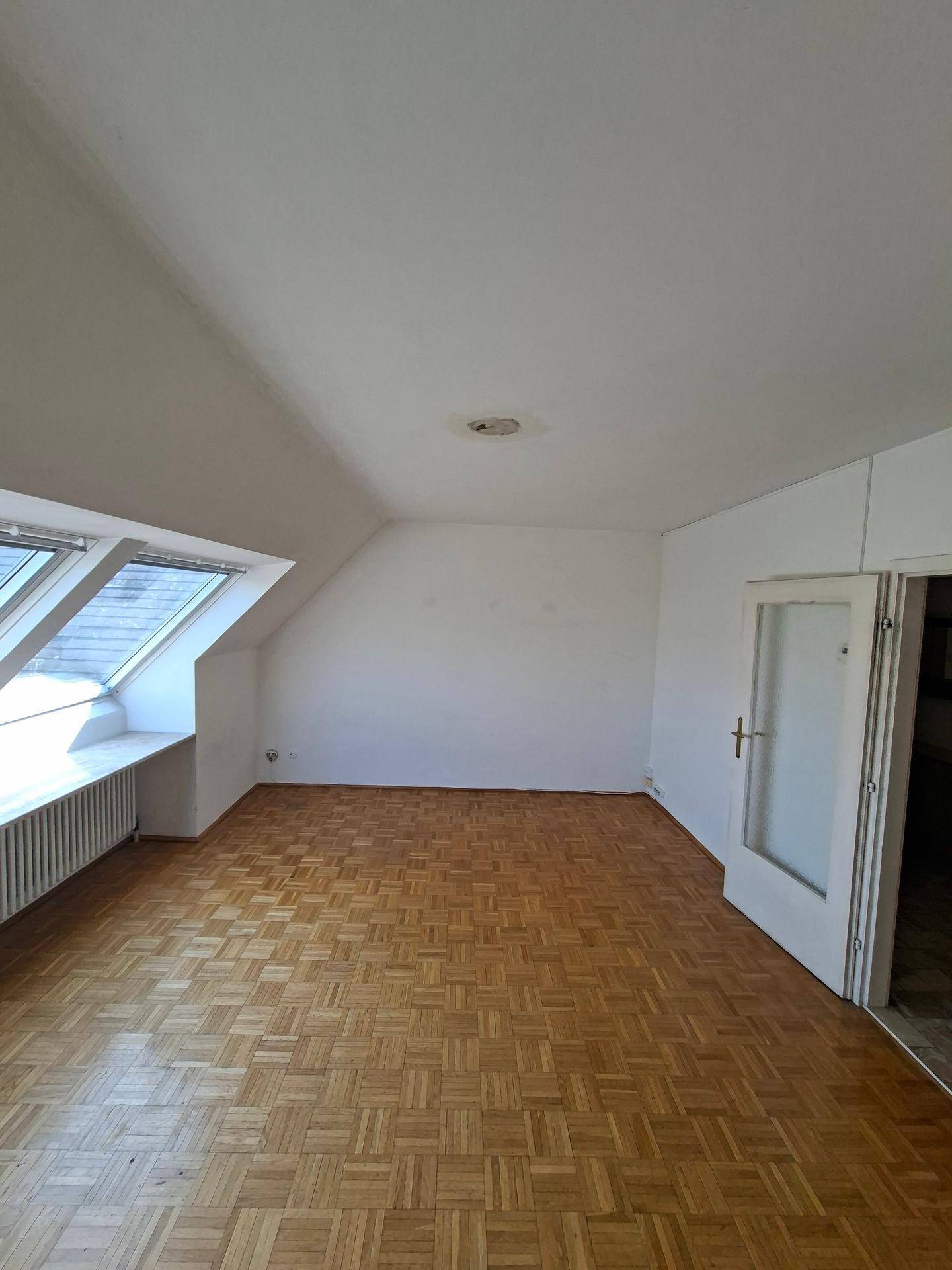 Geräumiges Dachzimmer mit Parkettboden, Dachfenstern und Zugang zu weiteren Räumen.