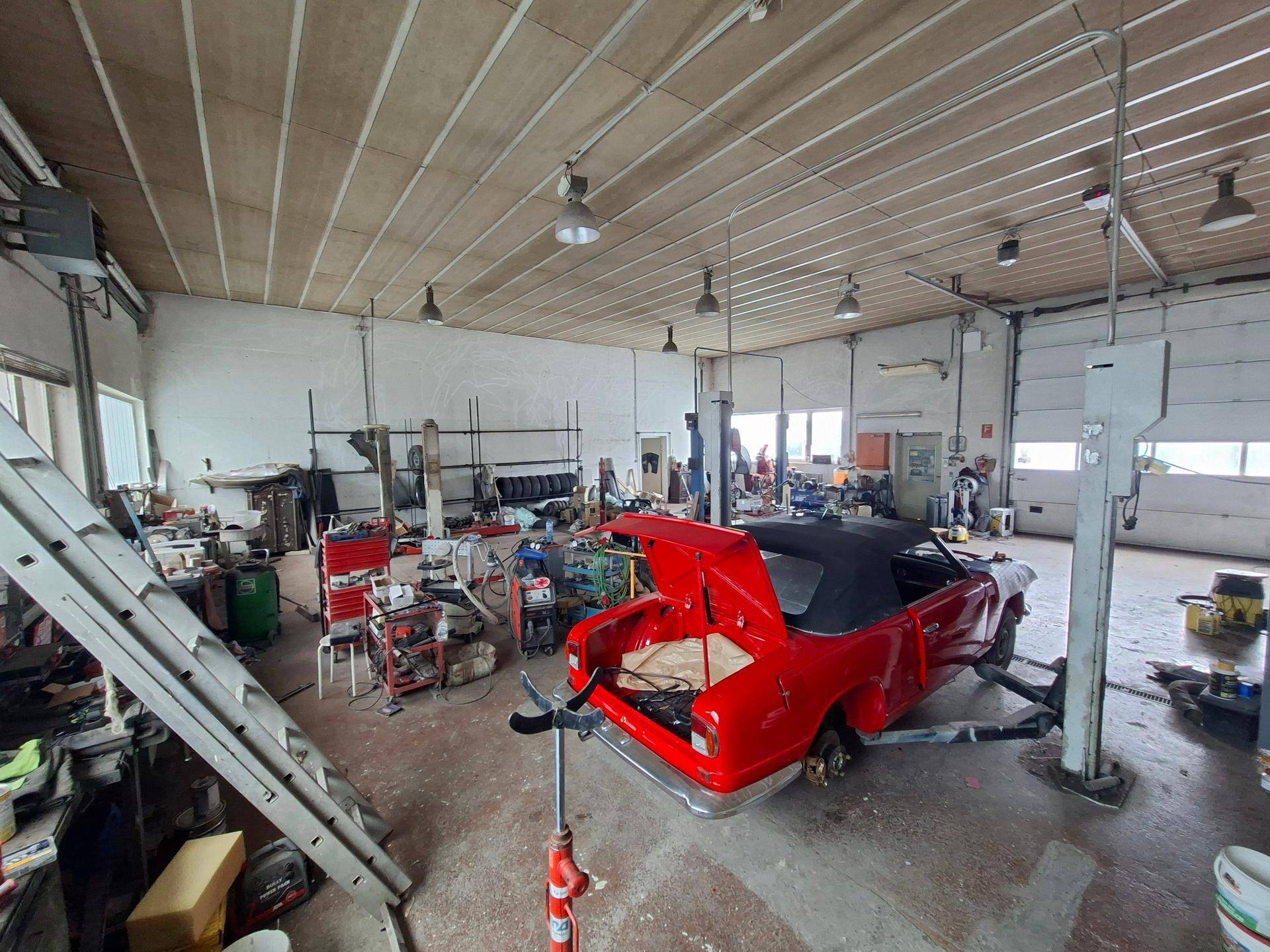Roter Oldtimer mit offenem Kofferraum auf einer Hebebühne in einer geräumigen Werkstatt.