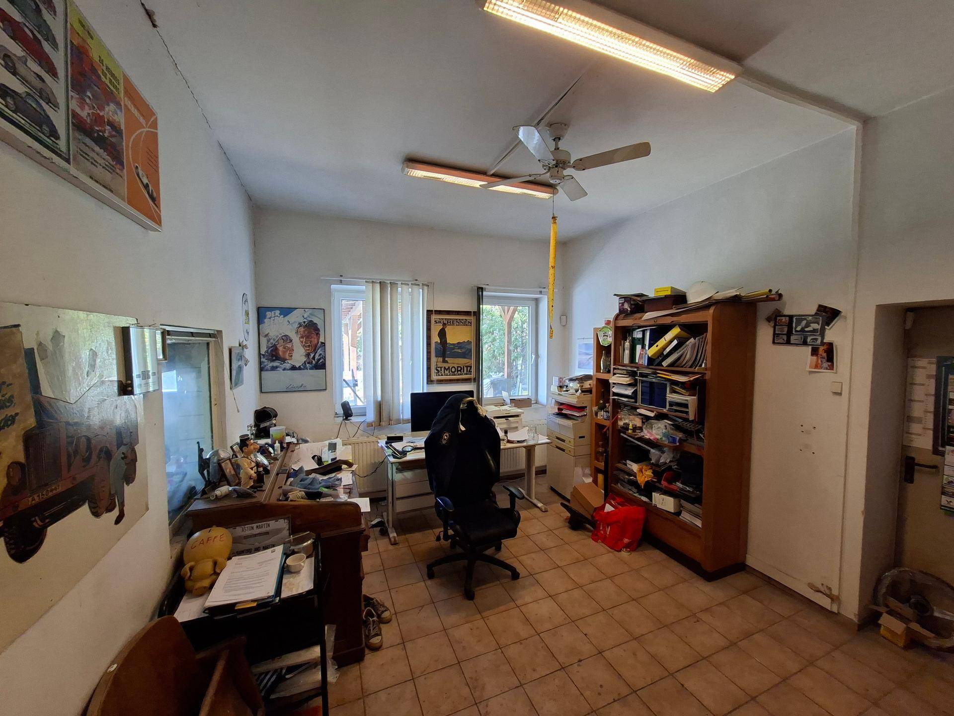 Büro mit Schreibtisch, Computer, Bürostuhl und Regalen, mit Blick ins Grüne.