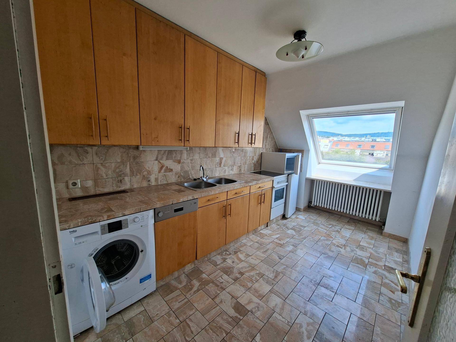 Küche mit Holzschränken, Fliesenboden, Einbaugeräten und Dachfenster.