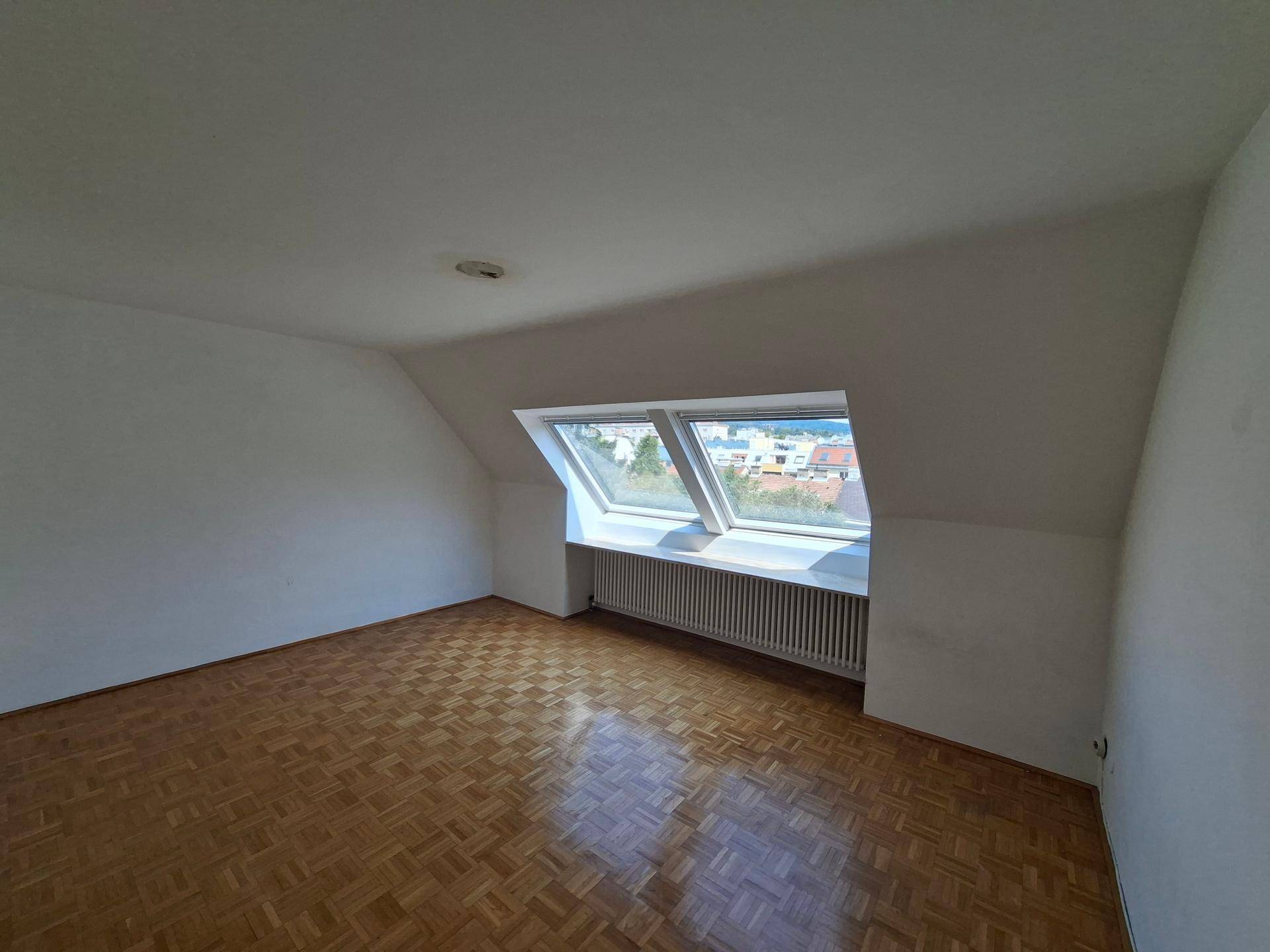Helles Dachzimmer mit Parkettboden und zwei großen Dachfenstern.