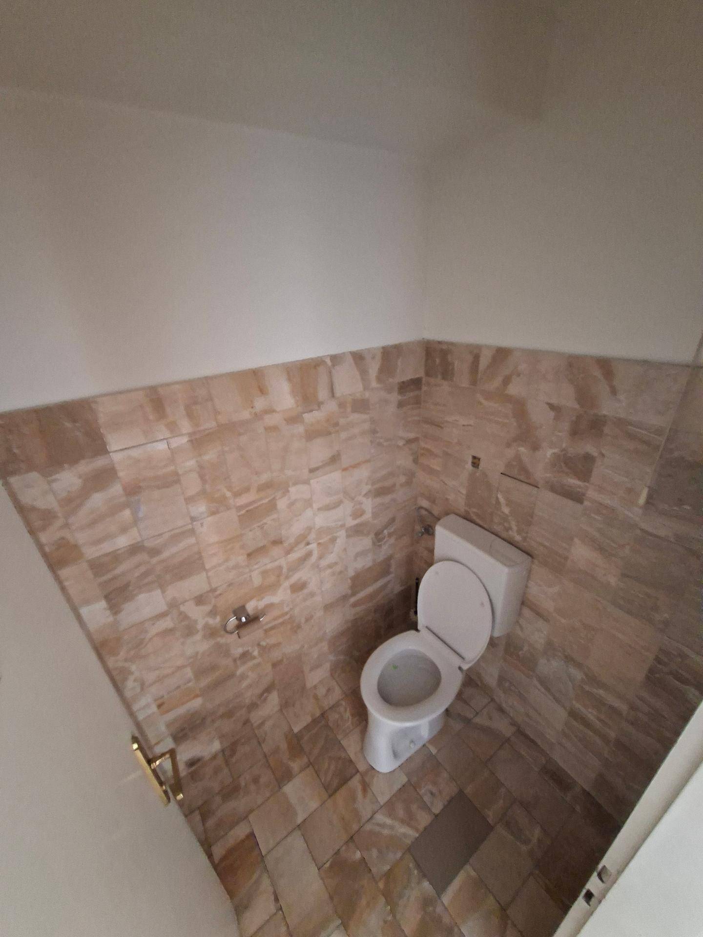 Separate Toilette mit WC und beigefarbenen Fliesen an Wänden und Boden.