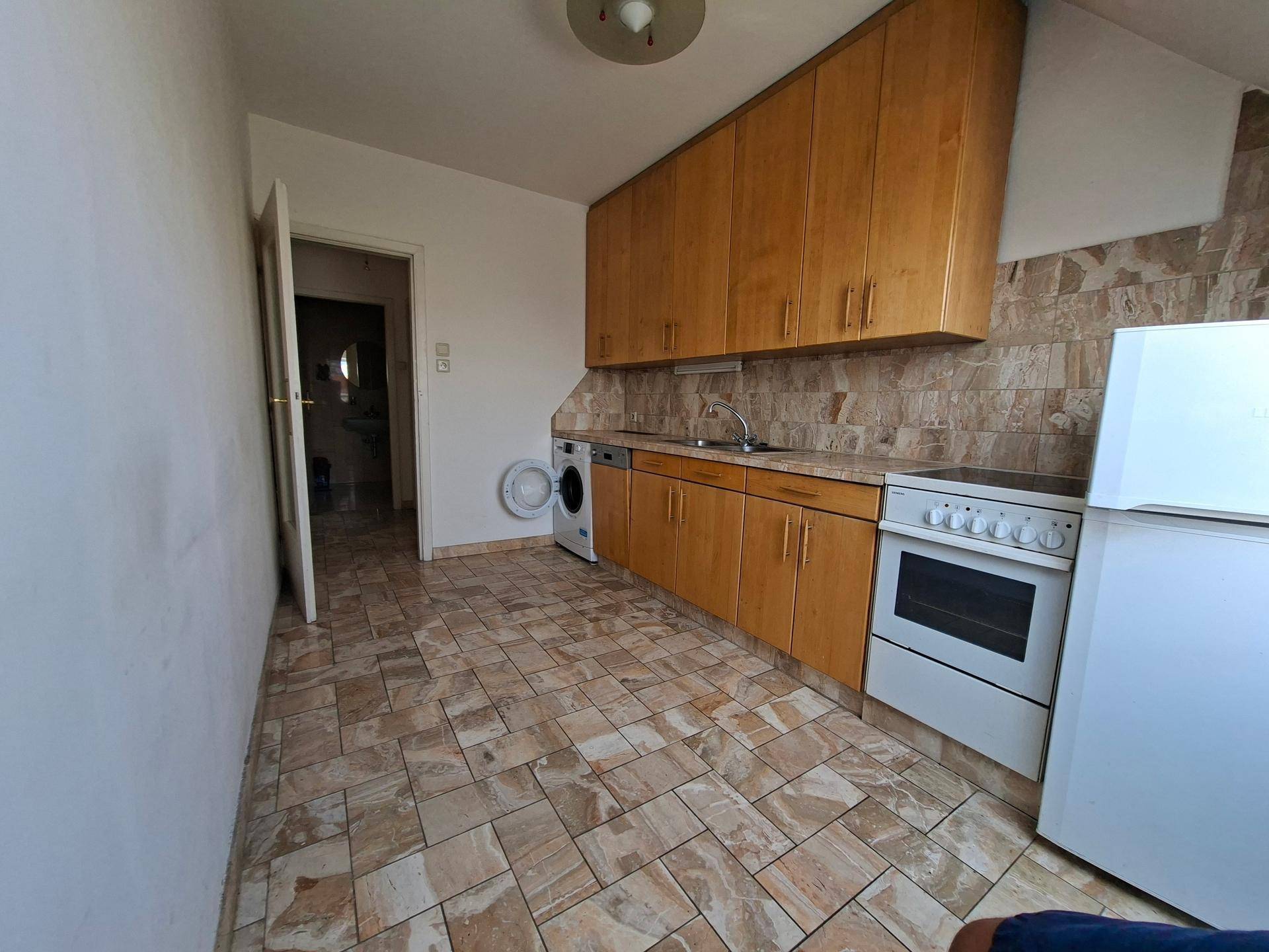 Funktionale Küche mit Holzfronten, Fliesenboden und grundlegenden Küchengeräten.