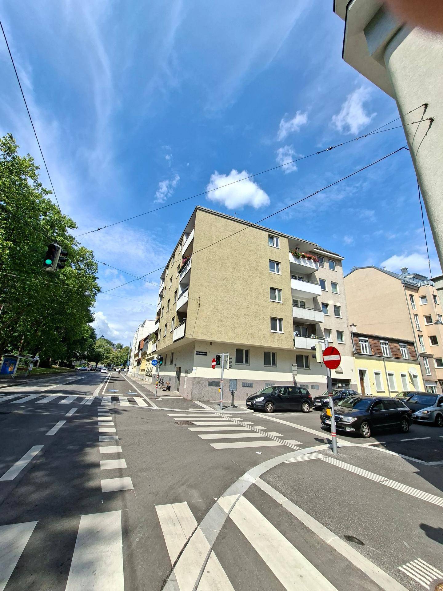 Wohngebäude an einer Kreuzung mit Fußgängerüberweg und umliegenden Häusern.