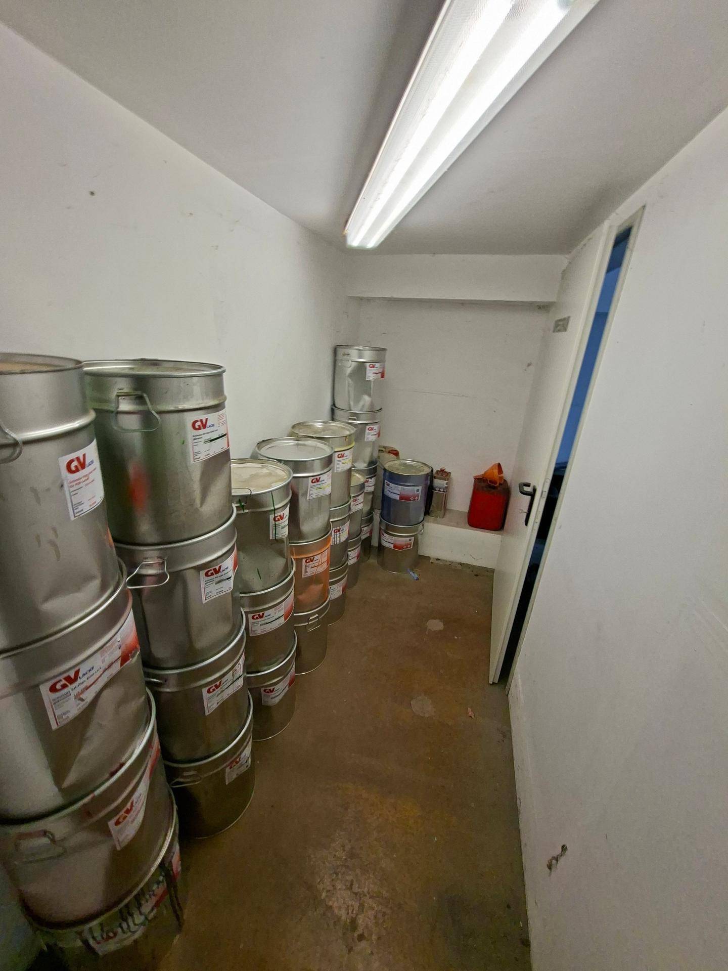 Lagerraum mit gestapelten Metallfässern, wahrscheinlich für Farben oder Chemikalien.