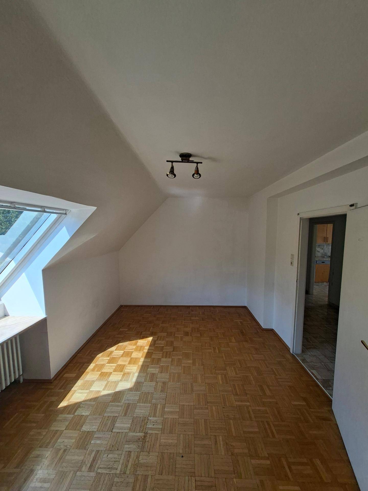 Lichtdurchflutetes Dachzimmer mit Parkettboden und Zugang zu angrenzenden Räumen.