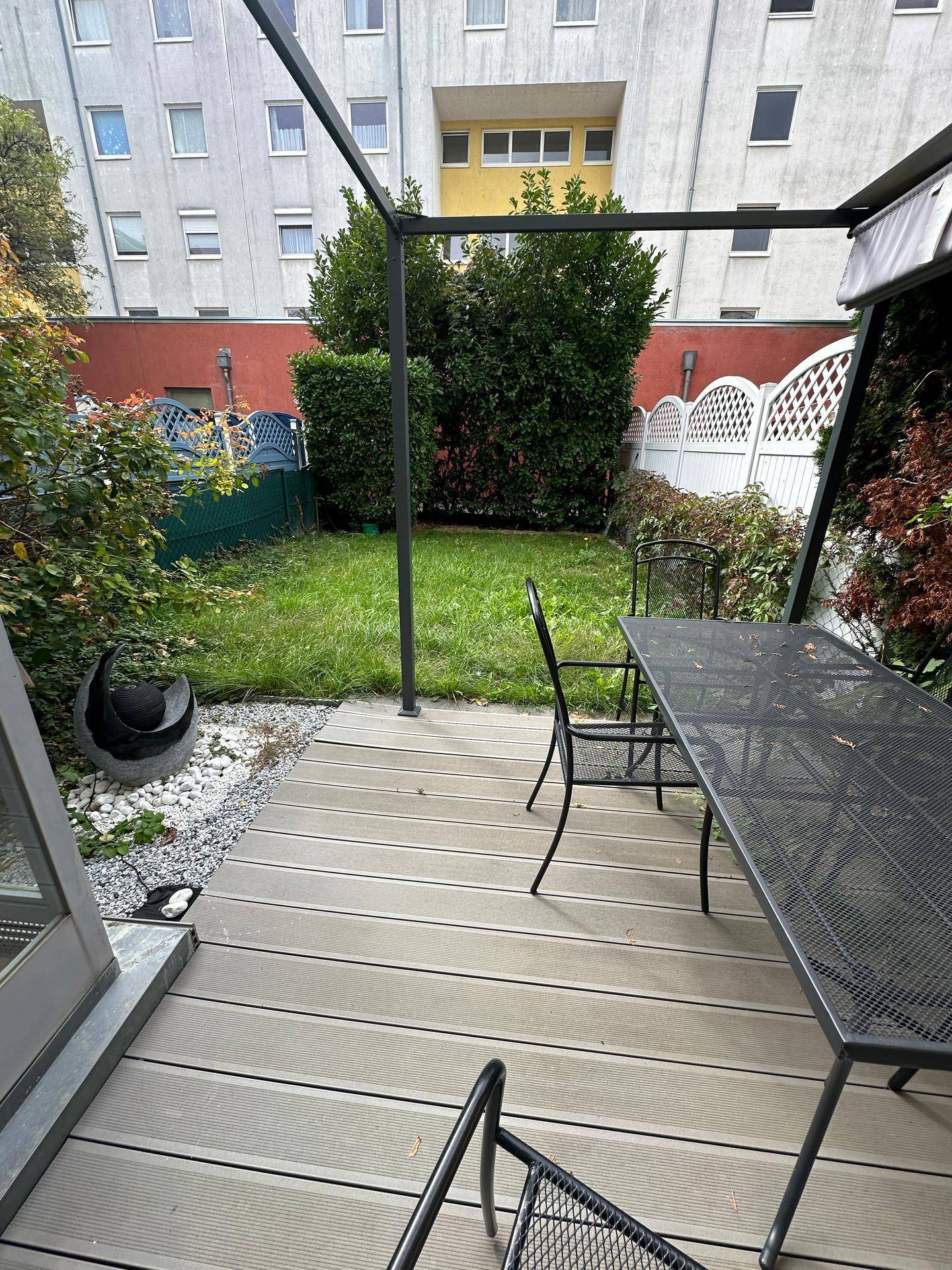 Terrasse mit Gartenmöbeln und Blick auf den gepflegten Garten und die umliegenden Gebäude.