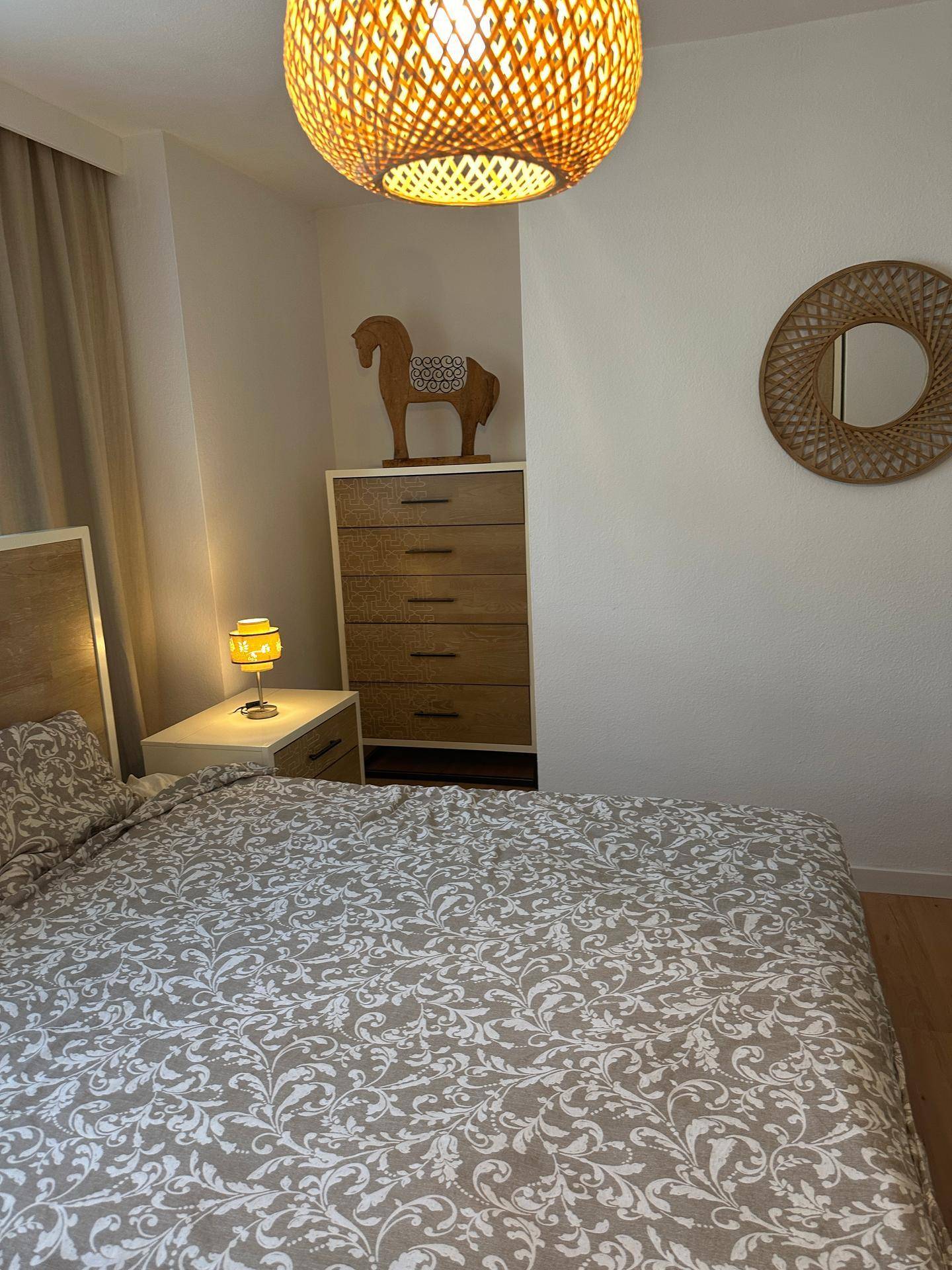 Schlafzimmer mit Nachttisch, Kommode und dekorativen Elementen.