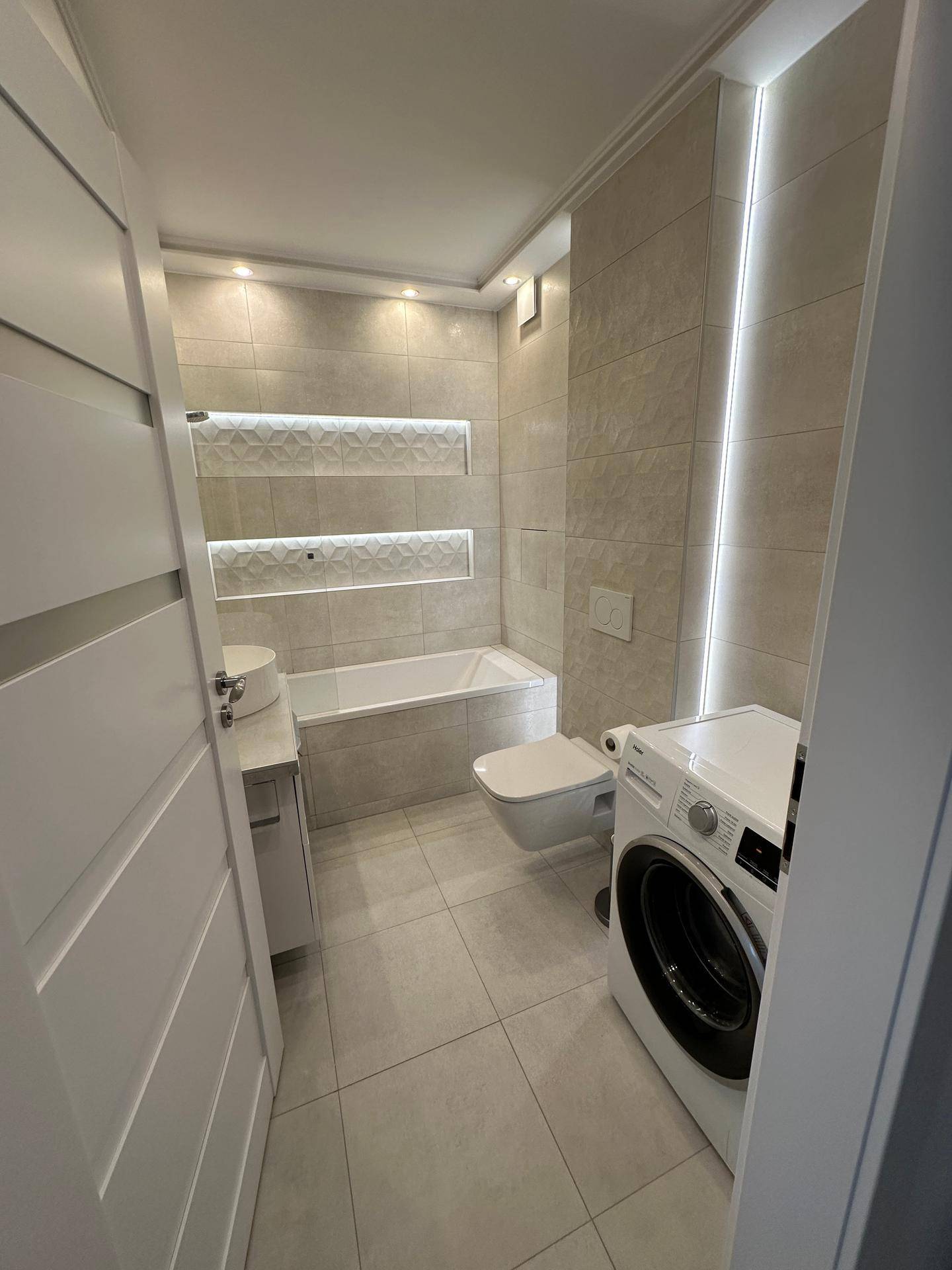 Modernes Badezimmer mit Badewanne, Wand-WC und integrierter Beleuchtung.