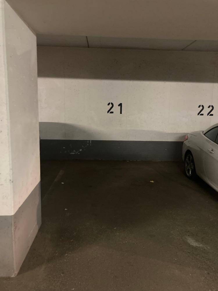 Tiefgaragenstellplatz Nummer 21 mit Betonwänden und -boden, ein Teil eines Autos ist sichtbar.