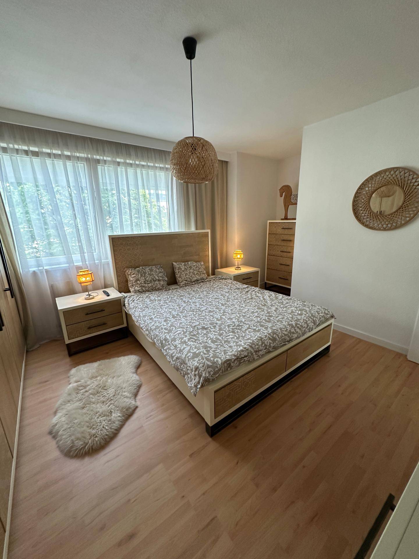 Helles Schlafzimmer mit Doppelbett, Holzmöbeln und großem Fenster.