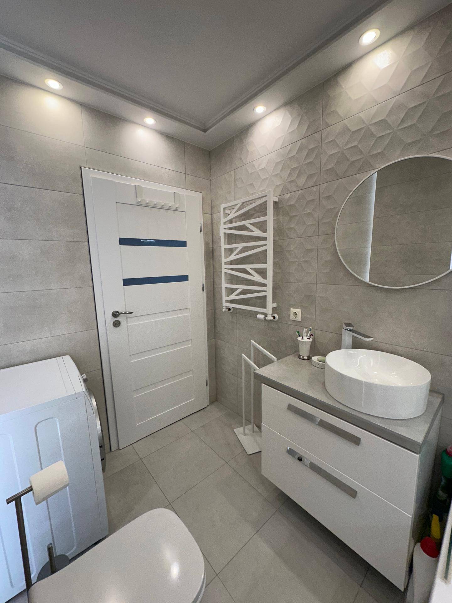 Badezimmer mit modernem Waschbecken, beleuchtetem Spiegel und beheiztem Handtuchhalter.