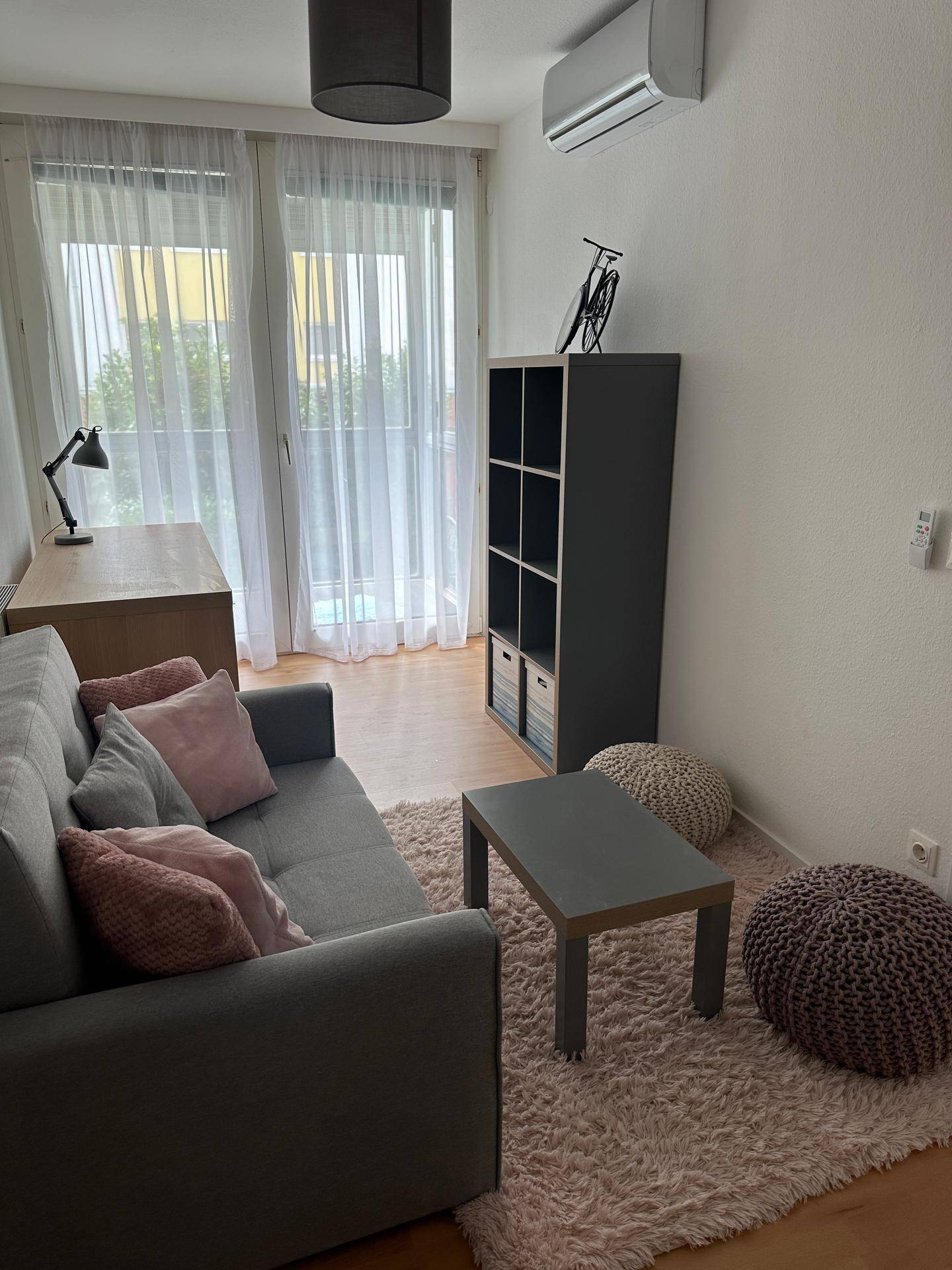 Gemütliches Zimmer mit Sofa, Schreibtisch und großem Fenster, das viel Licht hereinlässt.