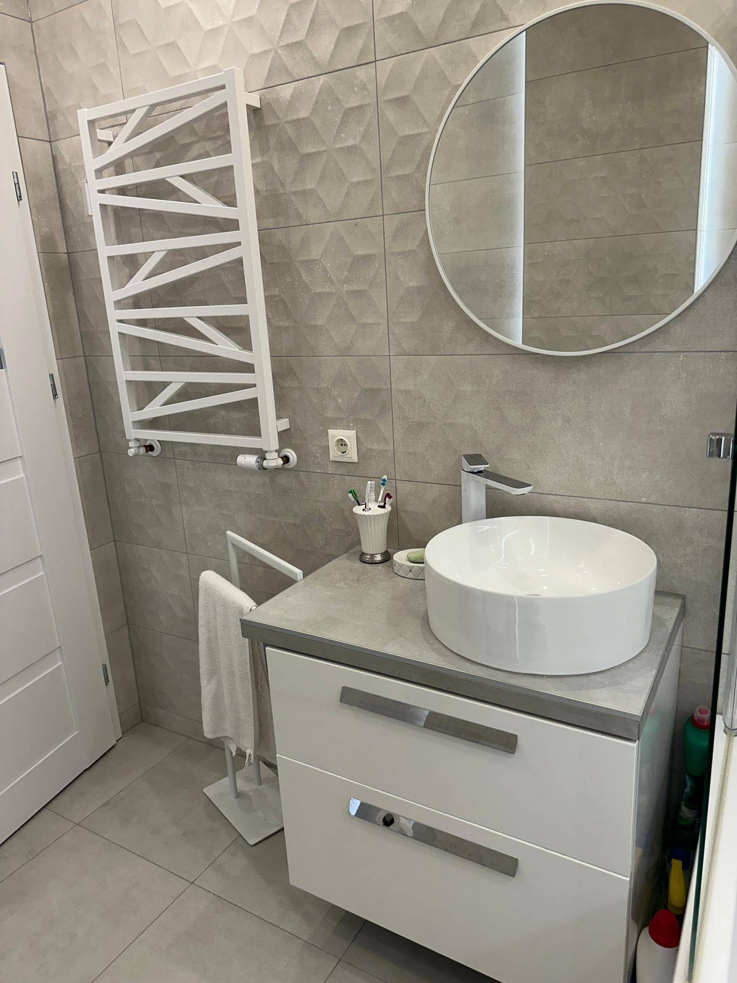 Modernes Badezimmer mit stilvollem Waschbecken, rundem Spiegel und grauen Fliesen.