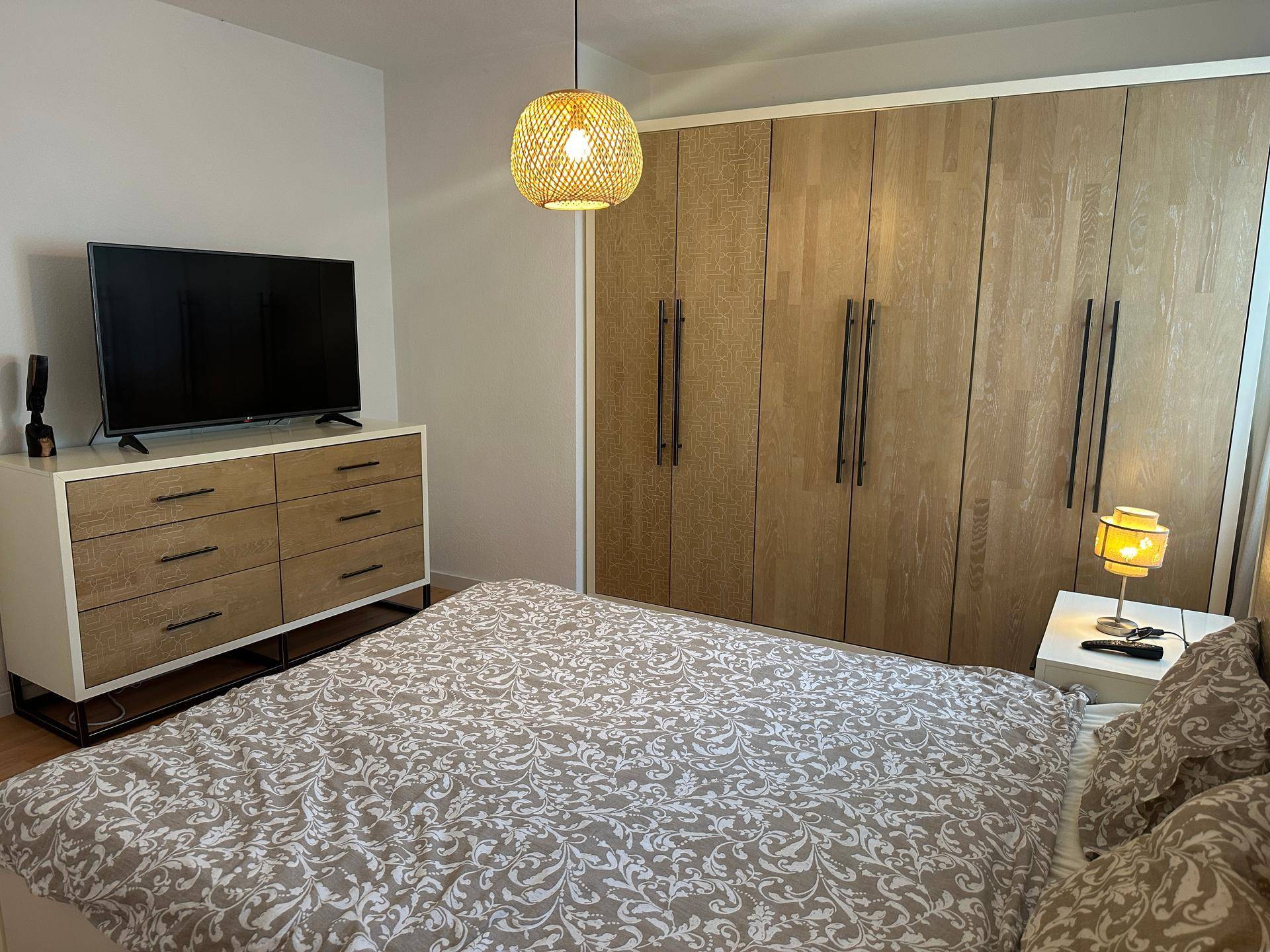 Schlafzimmer mit Fernseher auf einer Kommode und großem Einbauschrank.