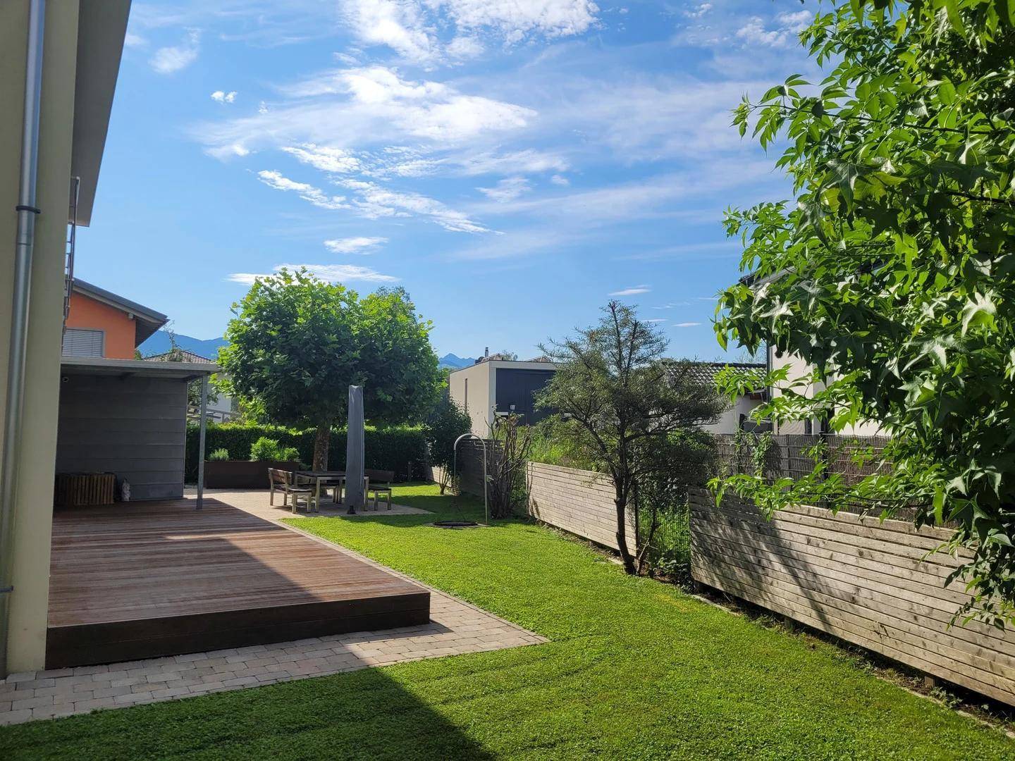 Sonniger Garten mit Holzterrasse und Blick auf die umliegende grüne Landschaft.