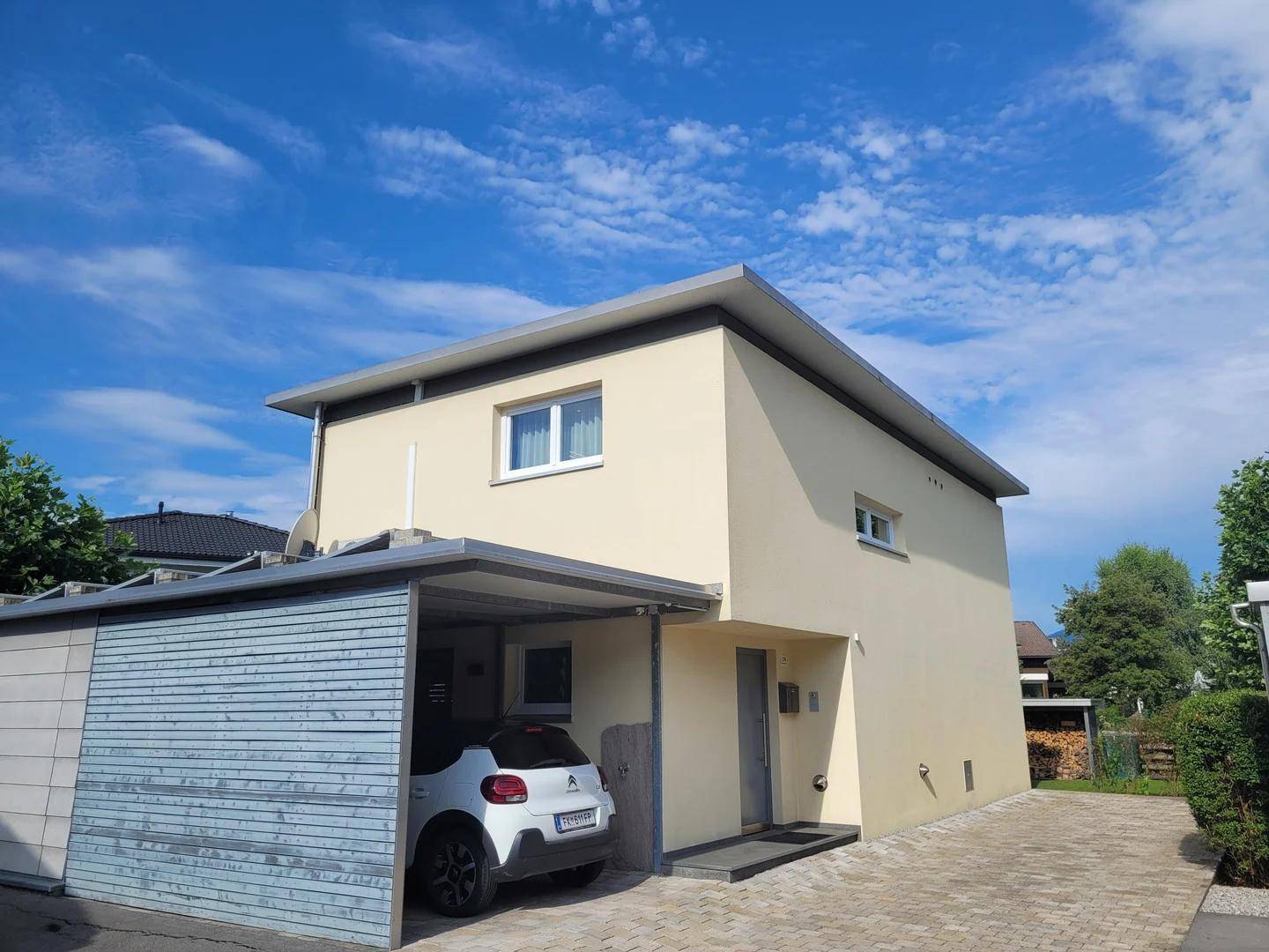 Moderne Hausfassade mit Carport und gepflasterter Einfahrt unter blauem Himmel.
