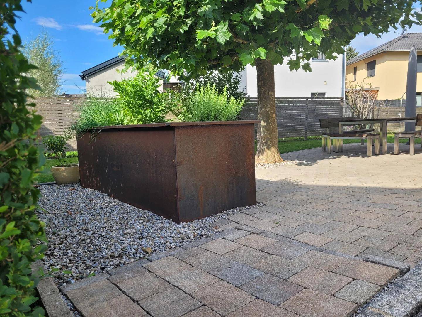 Gepflasterter Gartenbereich mit einem großen Pflanzgefäß und Sitzgelegenheiten im Freien.