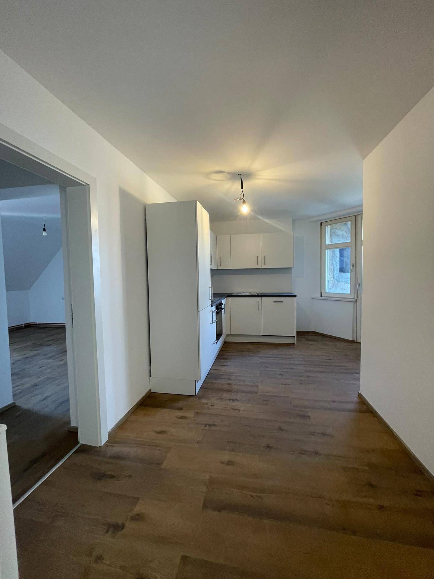 Helle Küche mit einfacher weißer Küchenzeile und modernem Laminatboden.