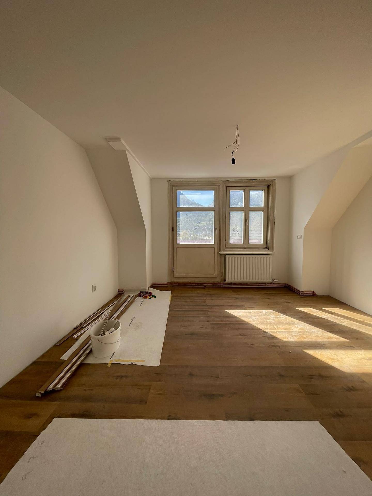 Heller Raum mit Laminatboden und Dachschräge, bereit für die Fertigstellung nach Renovierung.