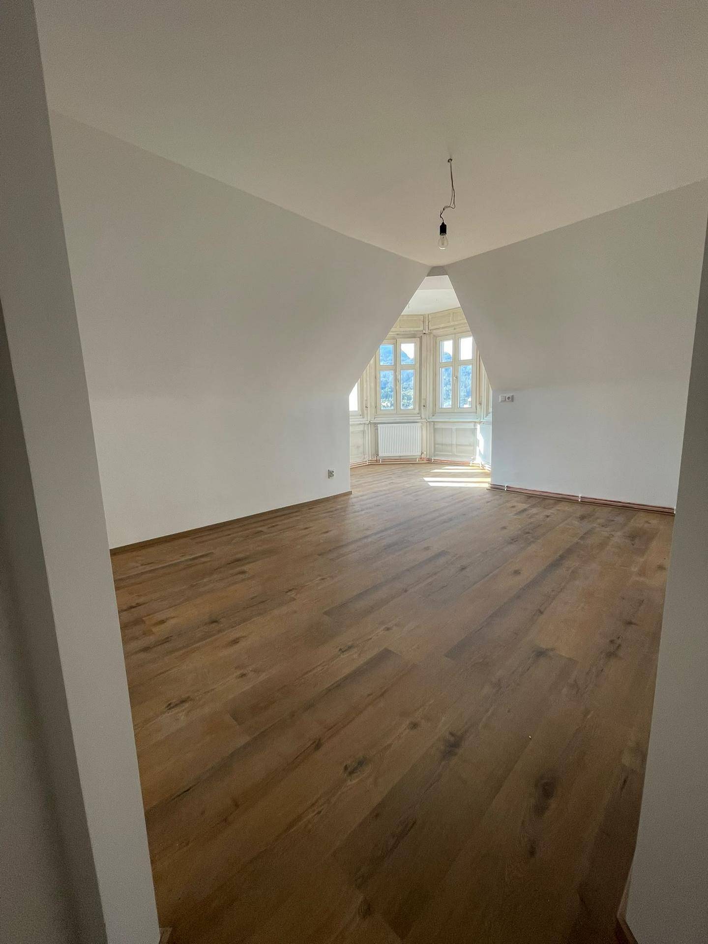 Geräumiger Wohnbereich mit Laminatboden, hellen Wänden und charakteristischen Erkerfenstern.