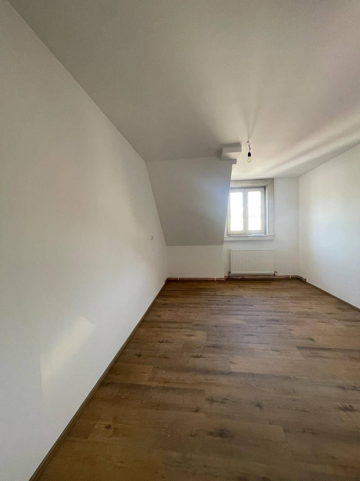 Heller Raum mit Laminatboden, weißen Wänden und Dachschräge, ideal als Schlafzimmer.