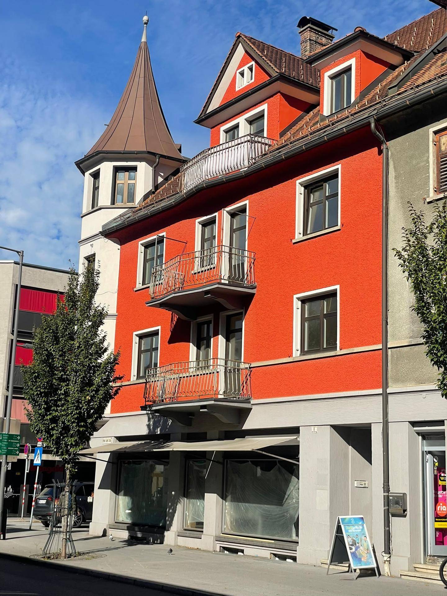 Detailansicht der roten Fassade des Eckgebäudes mit kleinen Balkonen und Turm.