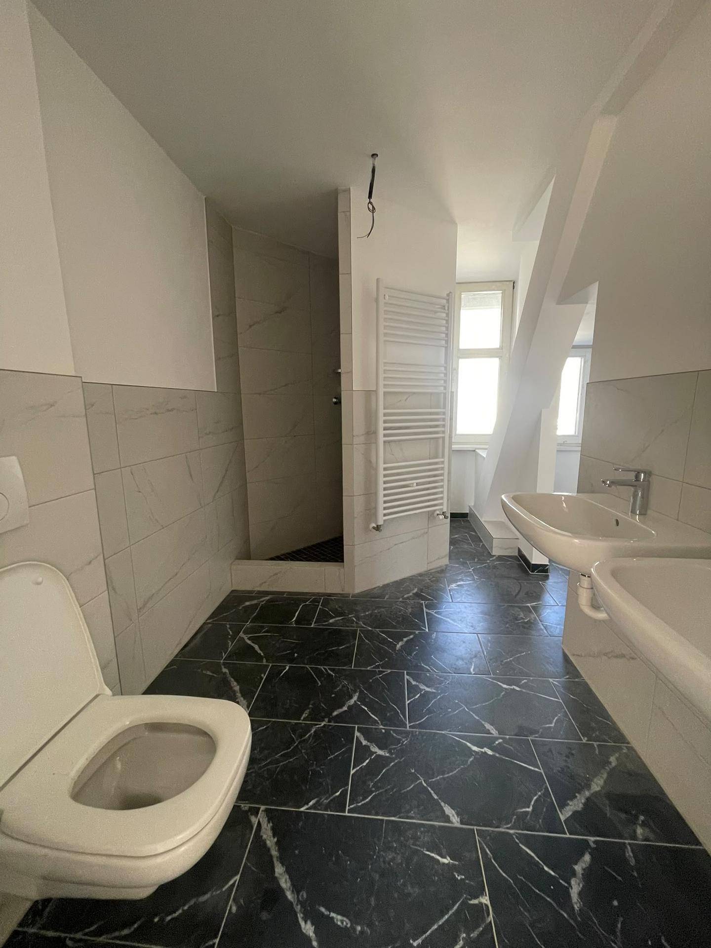 Modernes Badezimmer mit schwarz-weiß gefliestem Boden, Dusche und Dachschrägen.