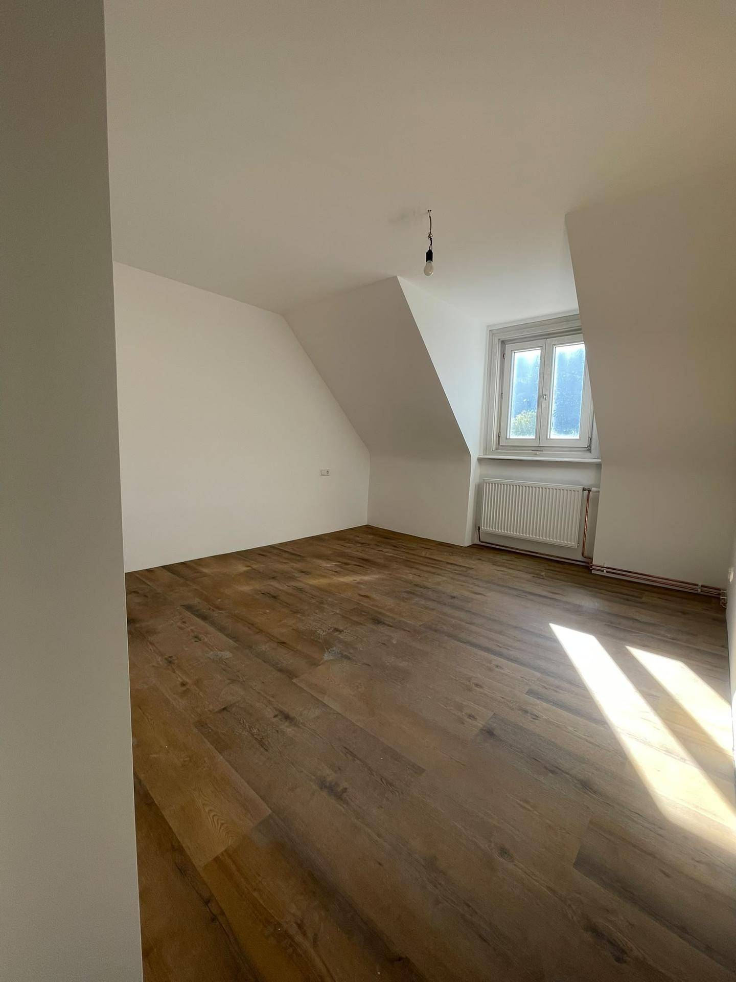 Lichtdurchfluteter Raum mit Laminatboden, weißen Wänden und Dachschräge, vielseitig nutzbar.