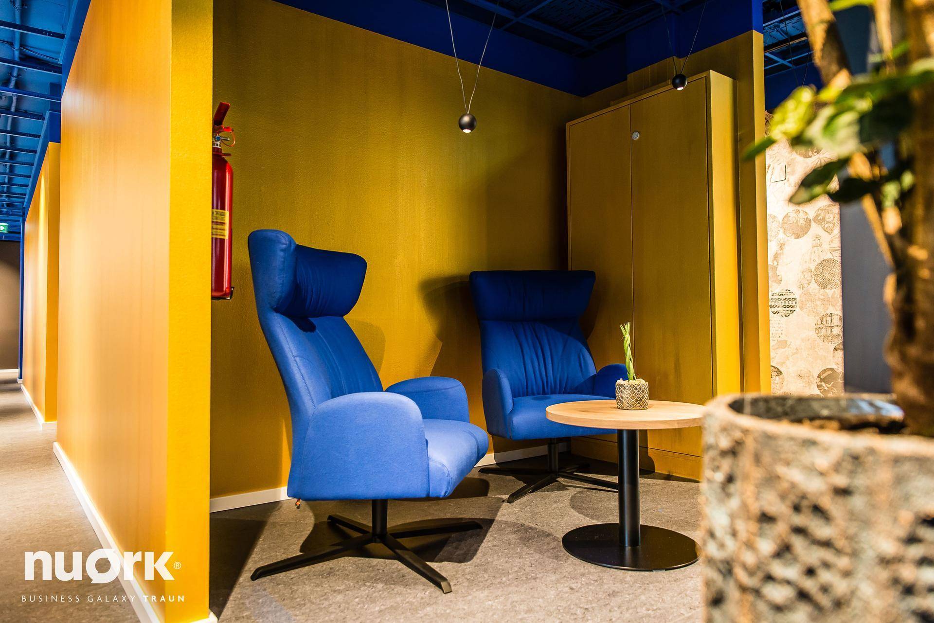 Lounge-Bereich mit blauen Sesseln, kleinem Tisch und Blick auf eine Bürotür, ideal für kurze Besprechungen.