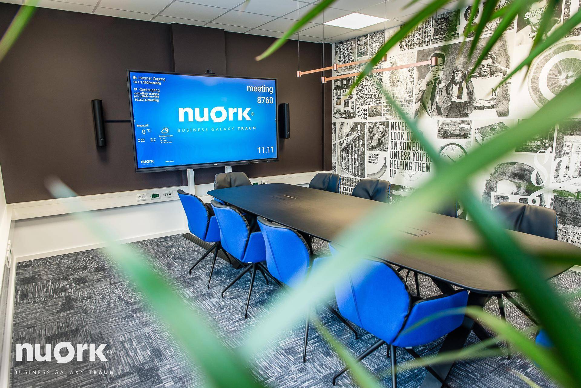Konferenzraum mit großem Bildschirm, blauen Stühlen und einer auffälligen Wand mit grafischen Mustern.