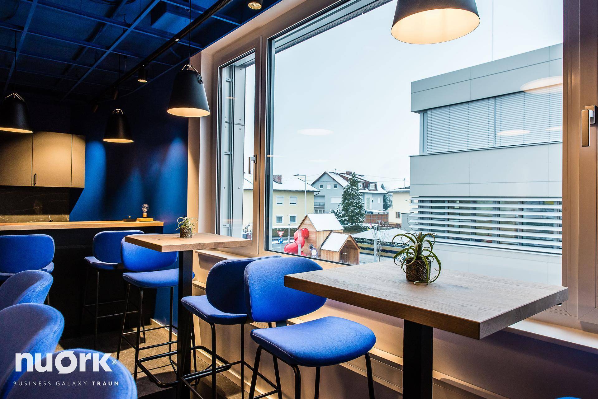 Gemütlicher Lounge-Bereich mit blauen Barhockern und einem weiten Blick aus dem Fenster auf die Straße.