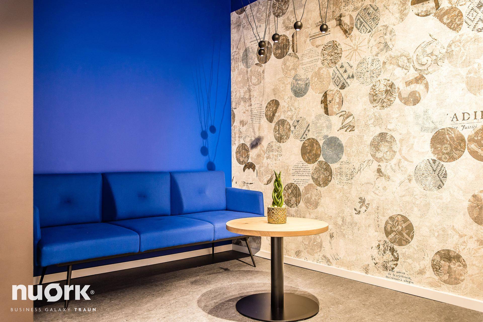 Moderner Lounge-Bereich mit blauen Sofas, hohen Tischen und Blick auf die Umgebung durch große Fenster.