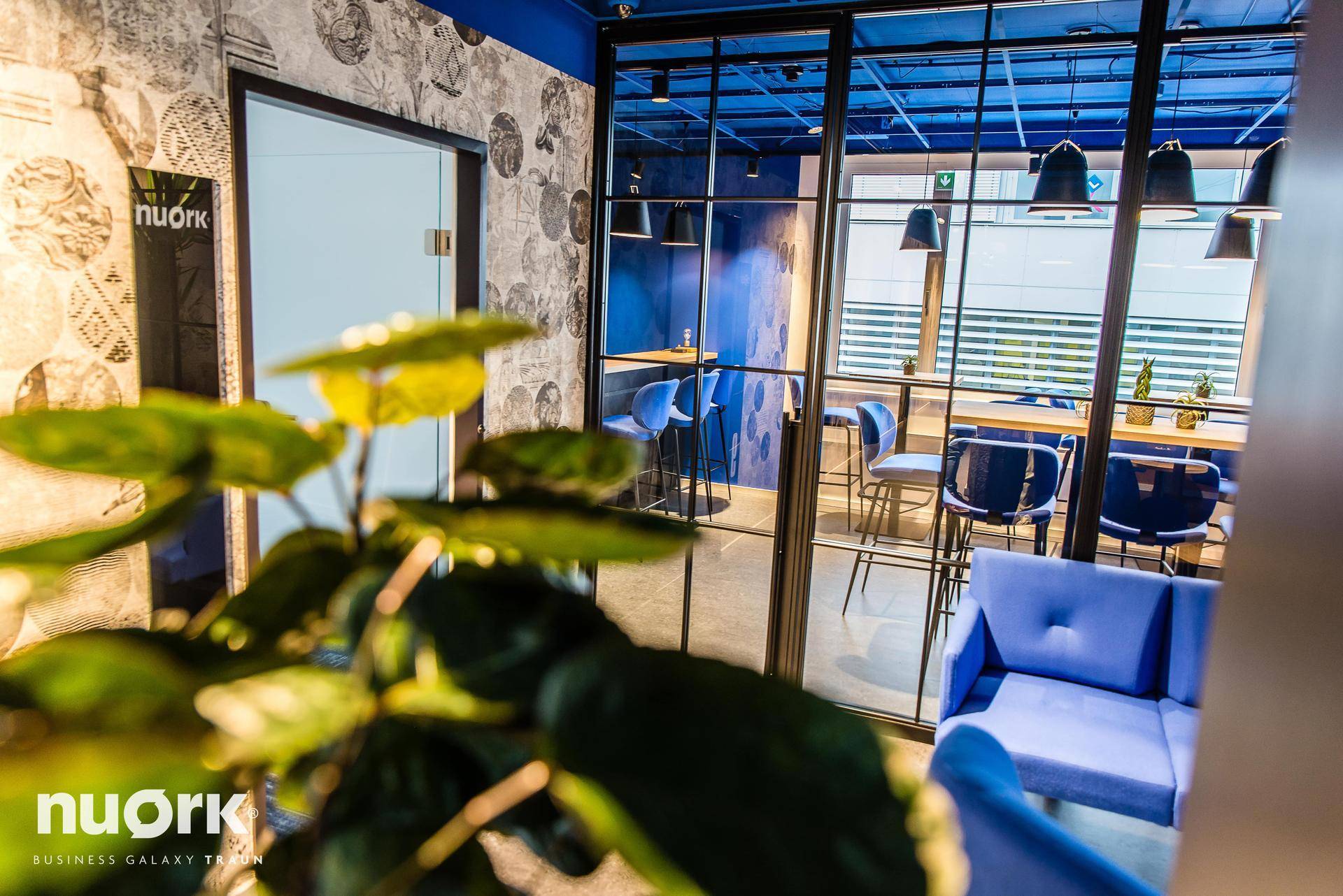 Moderner Lounge-Bereich mit blauen Sofas, hohen Tischen und Blick auf die Umgebung durch große Fenster.