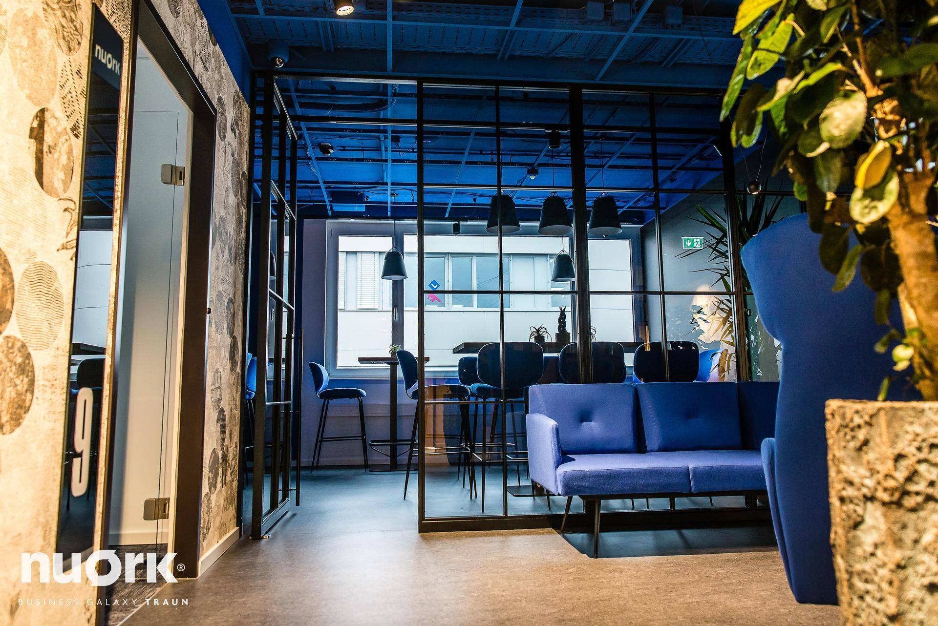 Detailansicht des Lounge-Bereichs mit blauem Sofa und Blick in den Barbereich, offen und modern.