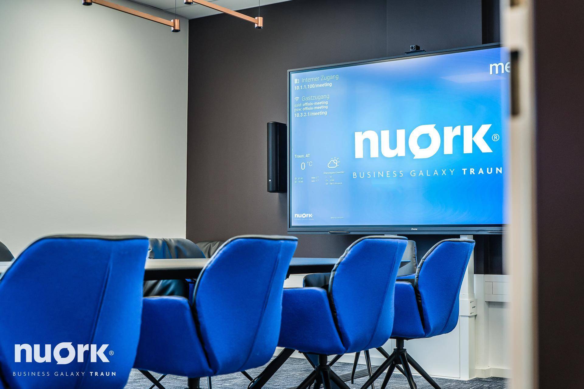 Moderner Konferenzraum mit großem Bildschirm, blauen Stühlen und Teppichboden für produktive Besprechungen.