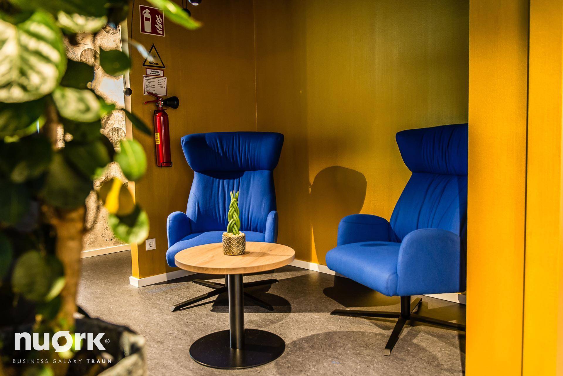 Moderner Lounge-Bereich mit blauen Sofas, hohen Tischen und Blick auf die Umgebung durch große Fenster.