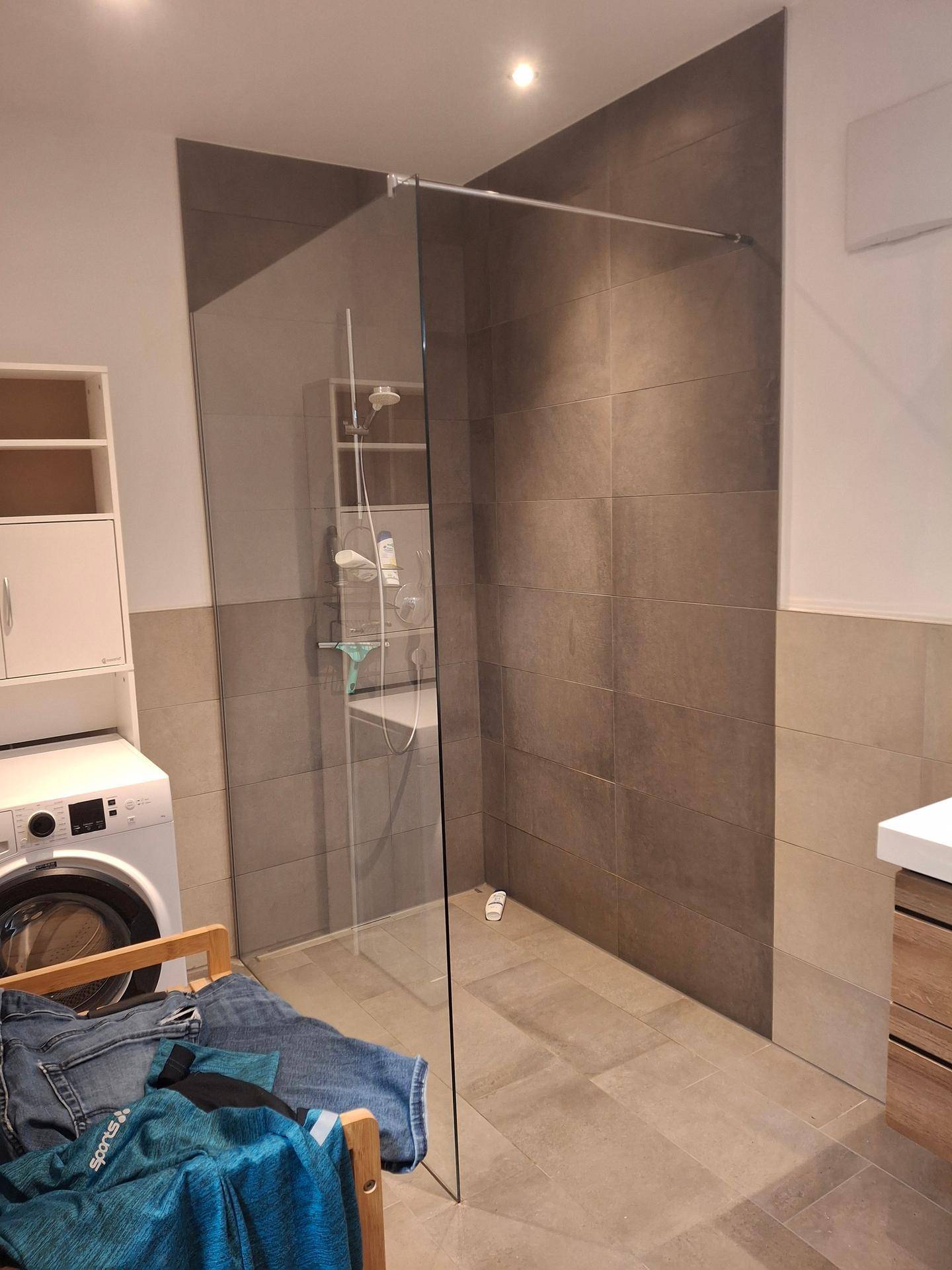 Modernes Badezimmer mit begehbarer Dusche, Waschmaschine und grauen Fliesen.
