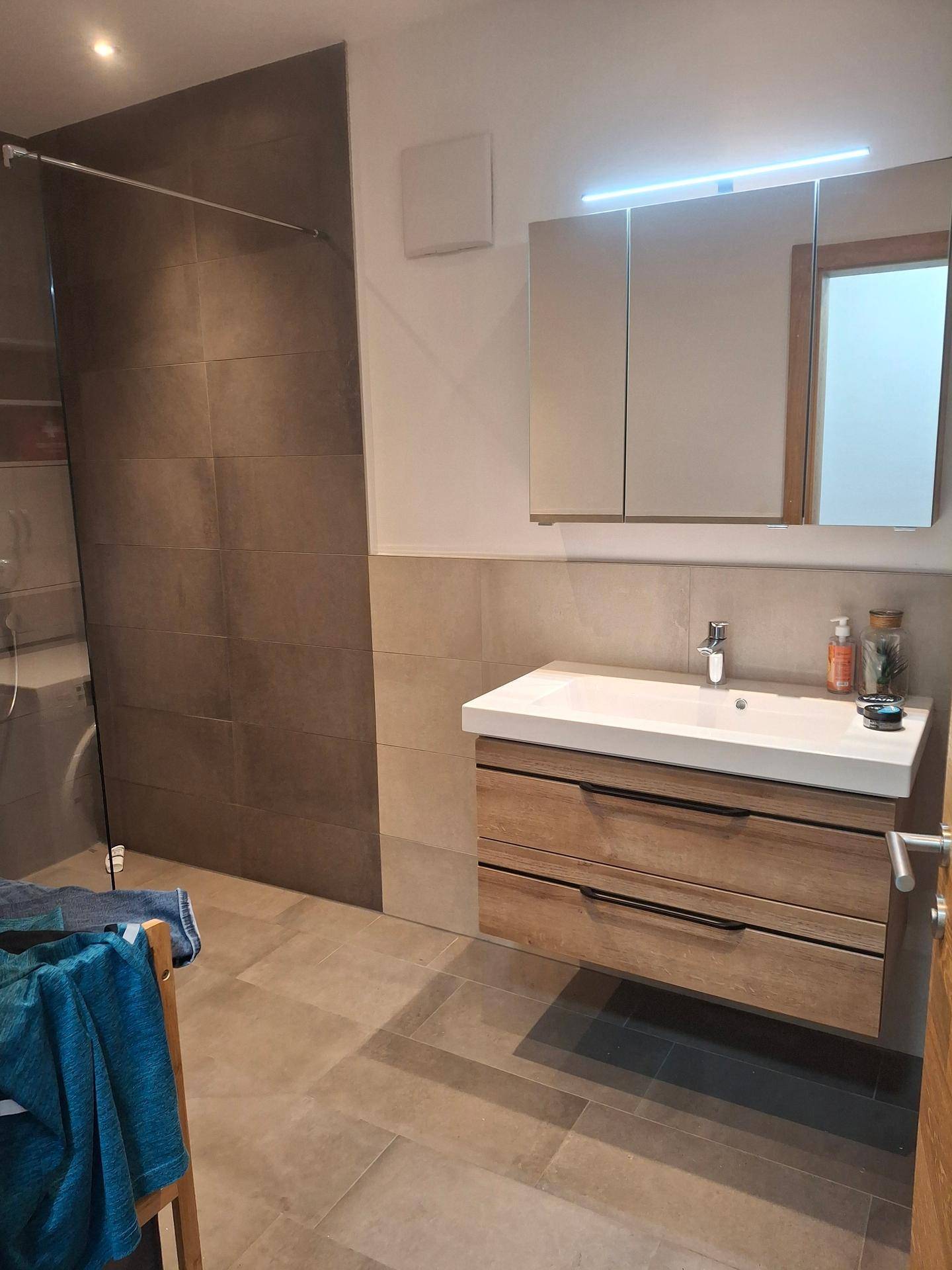 Helles Badezimmer mit modernem Waschtisch, Spiegelschrank und großer begehbarer Dusche.