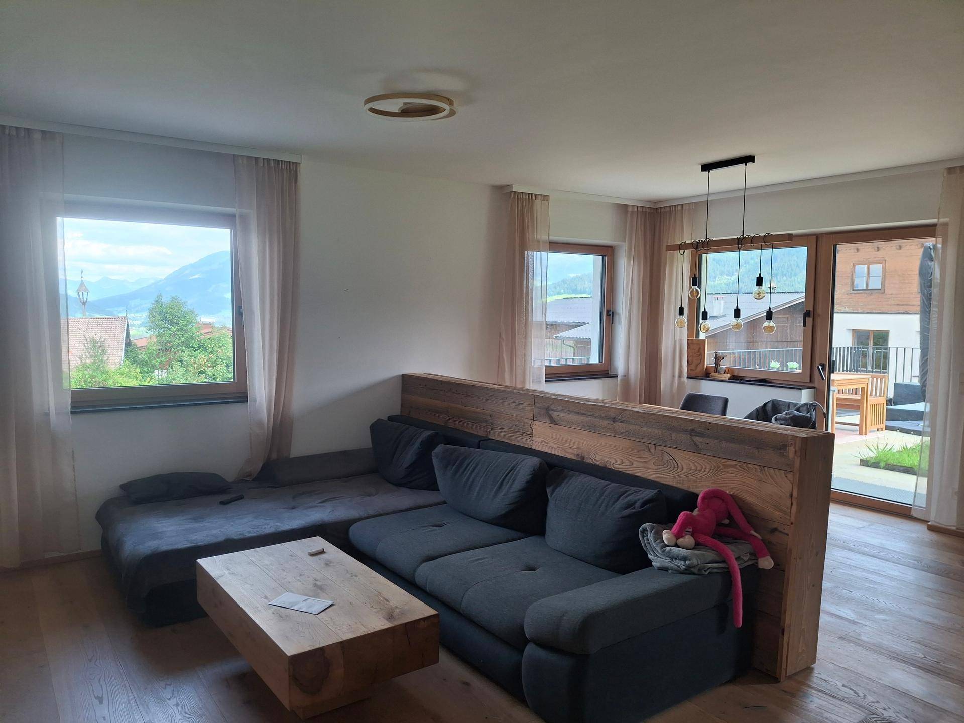 Gemütliches Wohnzimmer mit großem Sofa, Holztisch und Bergblick durch die Fenster.