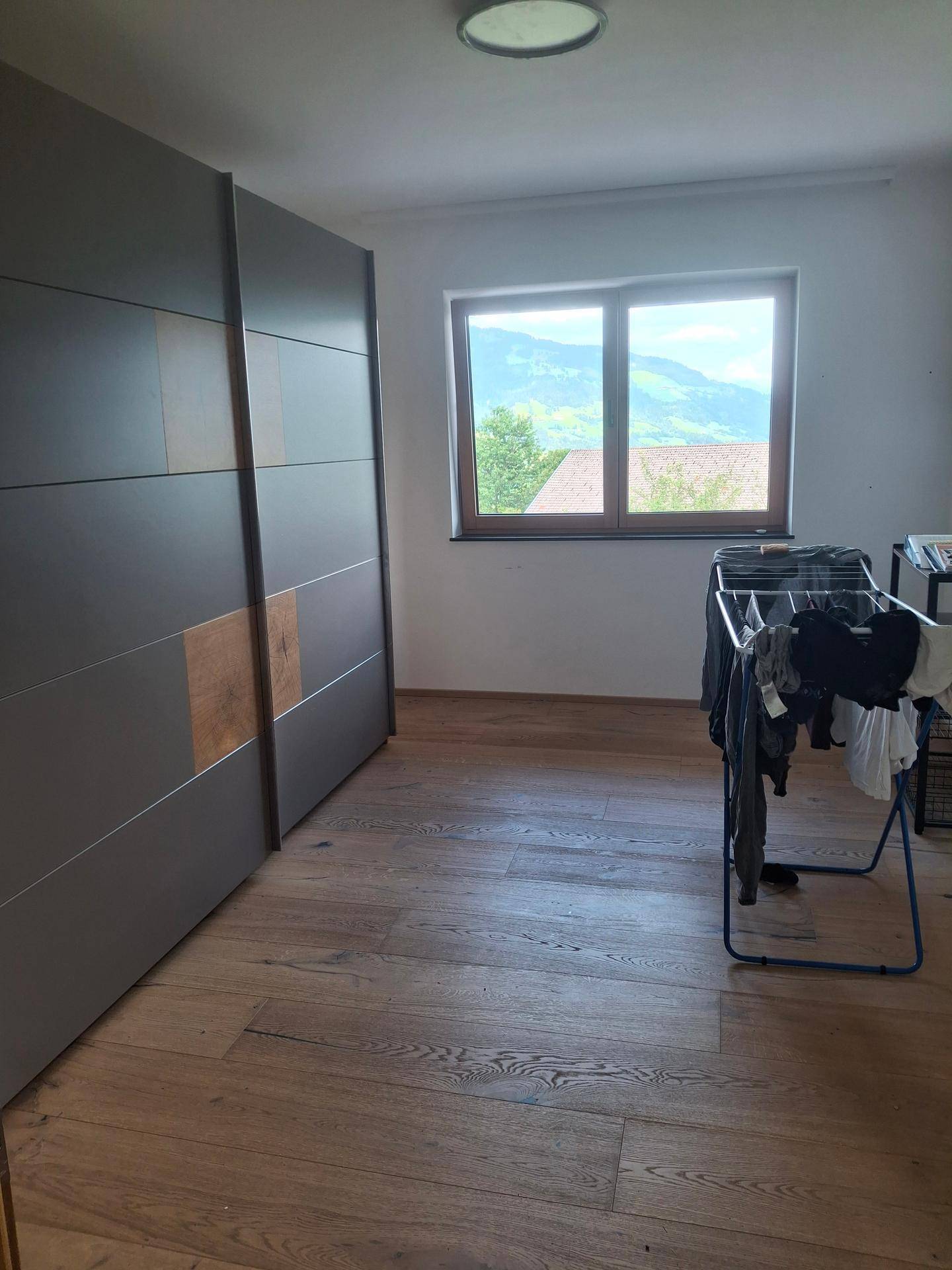 Schlafzimmer mit großem Einbauschrank, Holzboden und Fenster mit Bergblick.