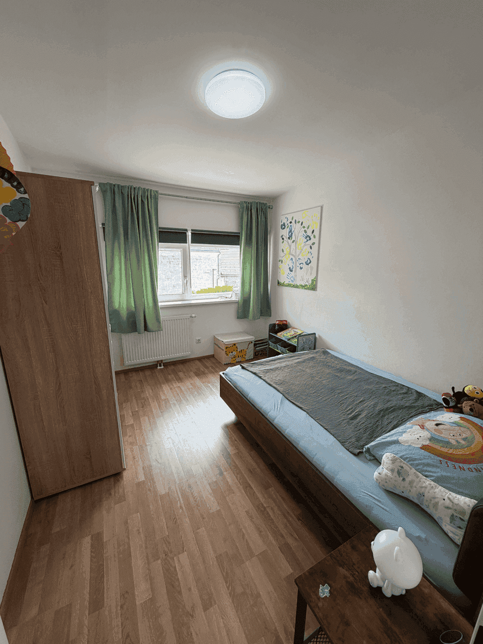 Kinderzimmer mit Einzelbett, Kleiderschrank und Laminatboden, hell und freundlich gestaltet.