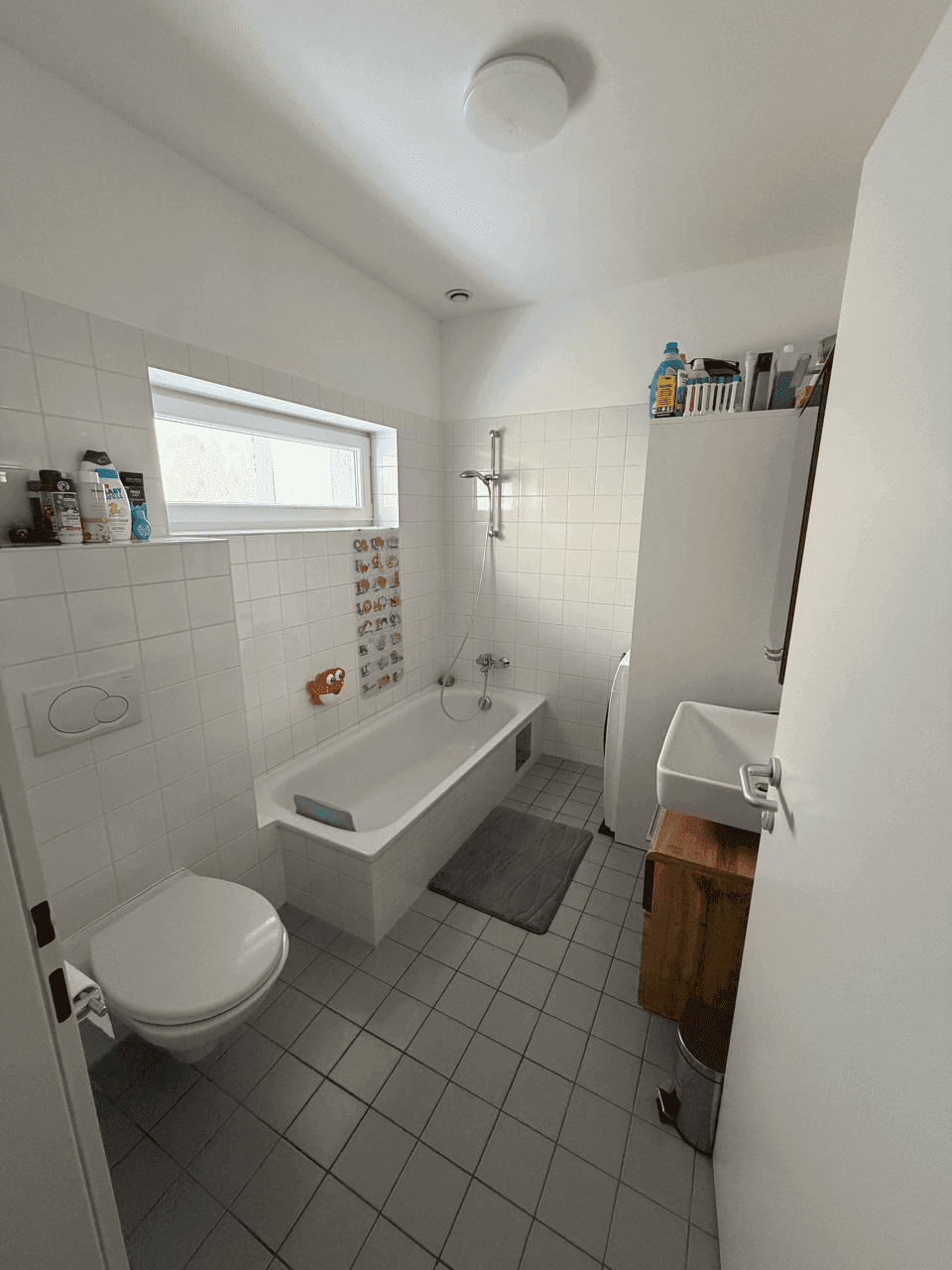 Badezimmer mit Badewanne, WC, Einzelwaschbecken und Fenster, funktional und hell gefliest.