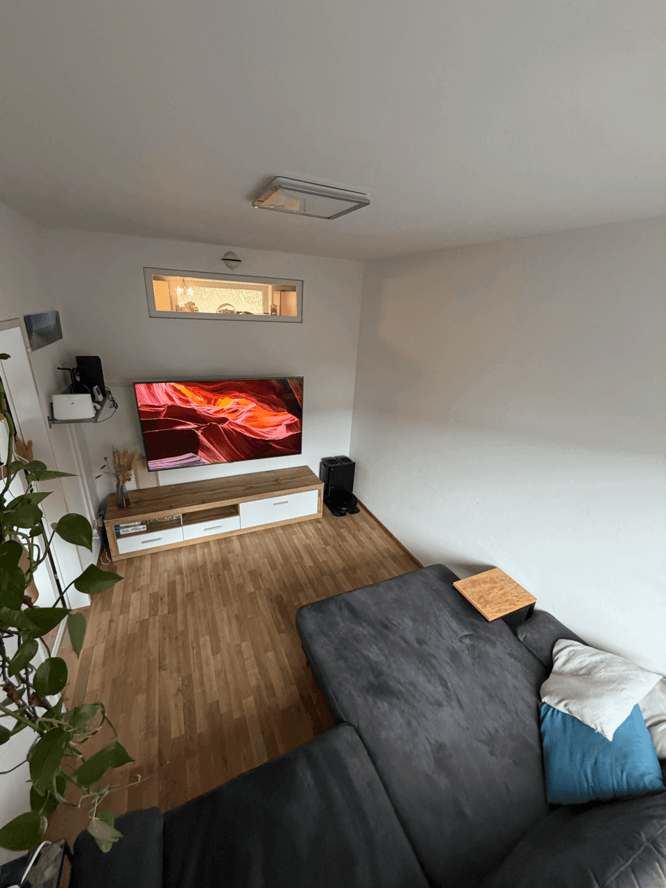 Helles Wohnzimmer mit großem Ecksofa, Fernseher und Laminatboden, ideal zum Entspannen.