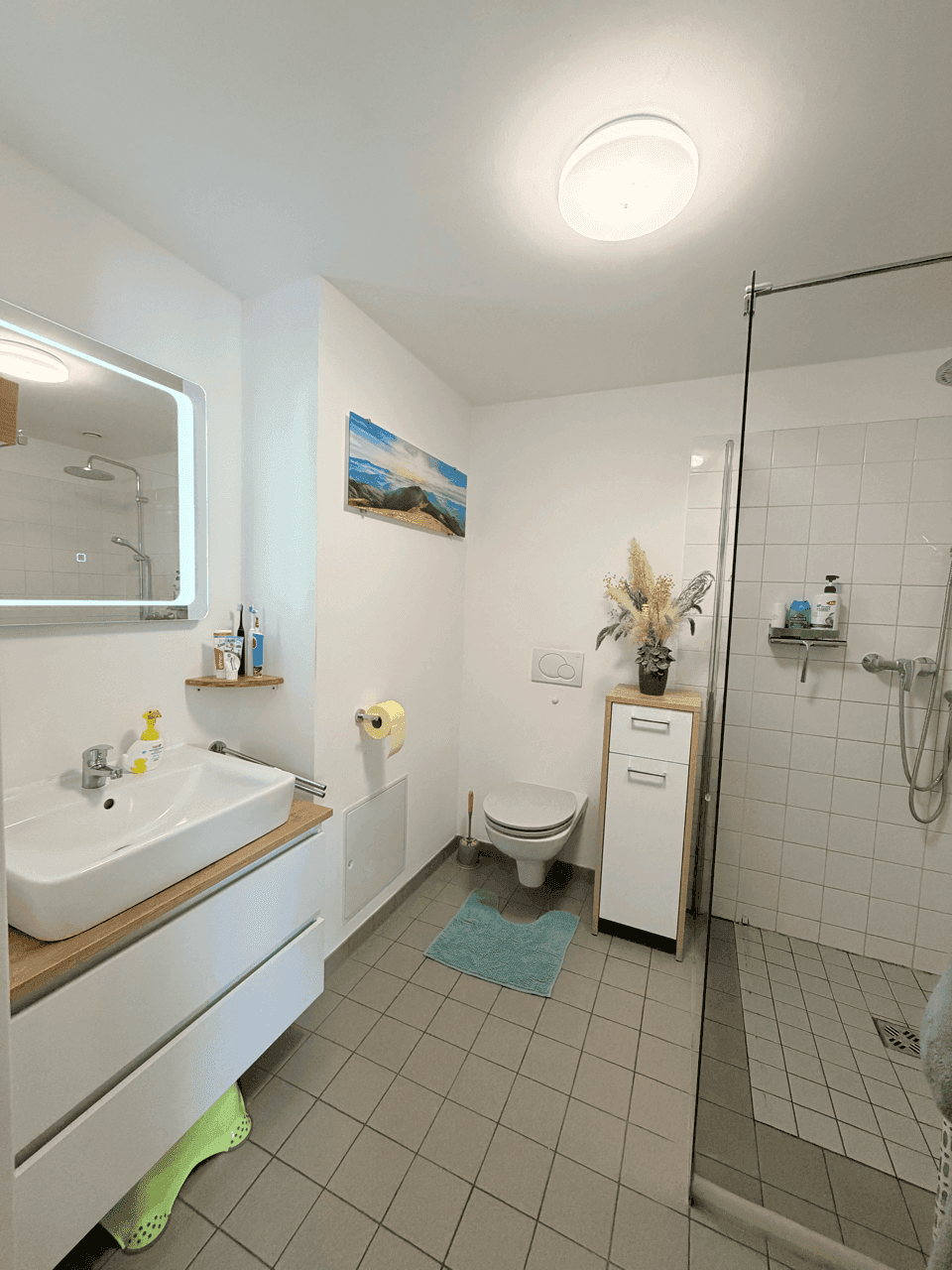 Modernes Badezimmer mit ebenerdiger Dusche, WC und Einzelwaschbecken, hell gefliest.