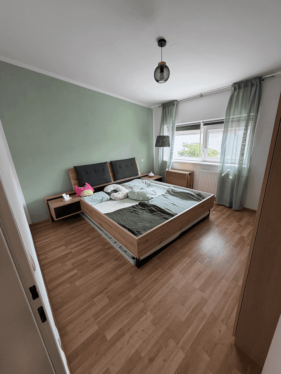 Gemütliches Schlafzimmer mit großem Holzbett, grüner Akzentwand und Laminatboden.